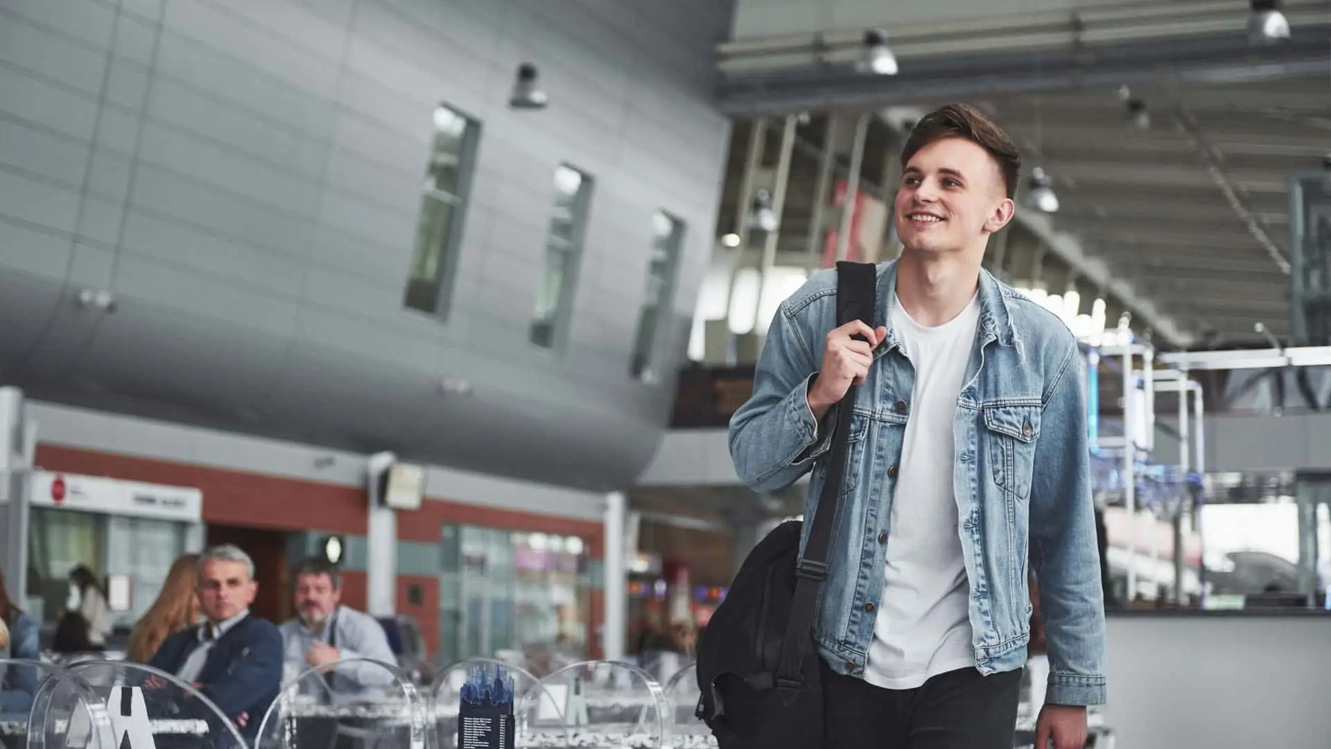 Joven viajero sonriente caminando por la terminal de un aeropuerto con su mochila.