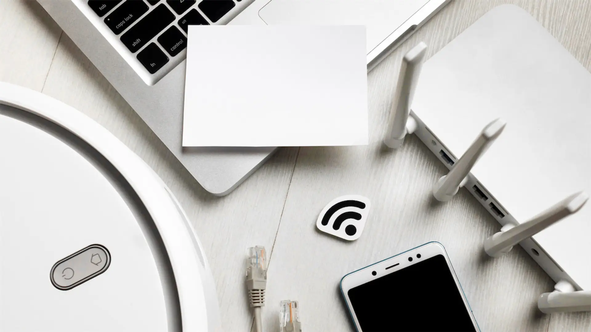 Adiós a la vuelta al cole: la mejor tarifa para ahorrar en internet y móvil durante todo el año Sobre una mesa se observan un portátil, un router, un teléfono móvil, cables de red y un símbolo de WiFi, ilustrando los servicios de internet y comunicaciones en el hogar.