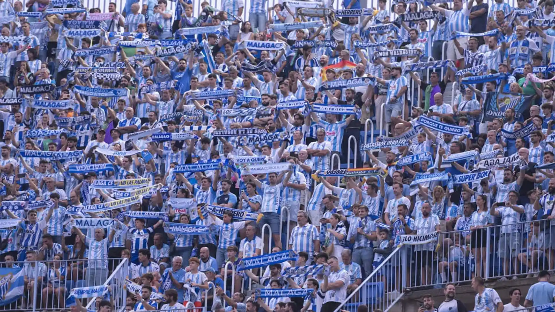 Afición del Málaga CF en la grada con bufandas y camisetas azules y blancas