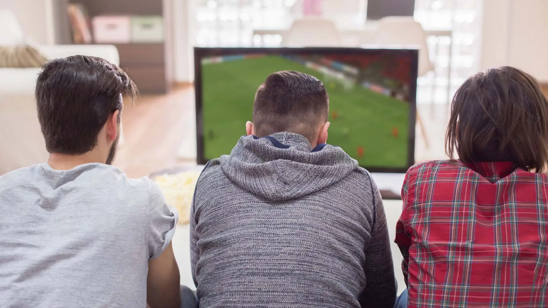 Grupo de amigos de espaldas viendo un partido de fútbol en la televisión.