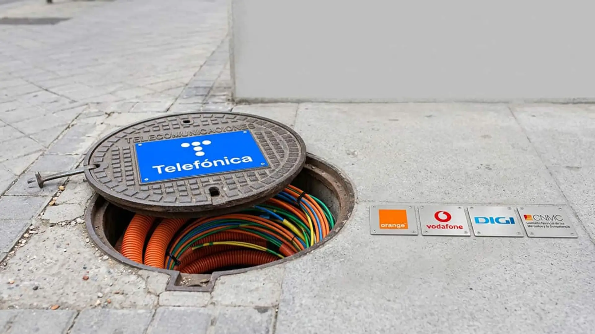 Orange, Vodafone y Digi, contra Telefónica ante la CNMC por subir un 116,4% sus conductos en cinco años Arqueta de telecomunicaciones de Telefónica con cables y logotipos de Orange, Vodafone, Digi y CNMC