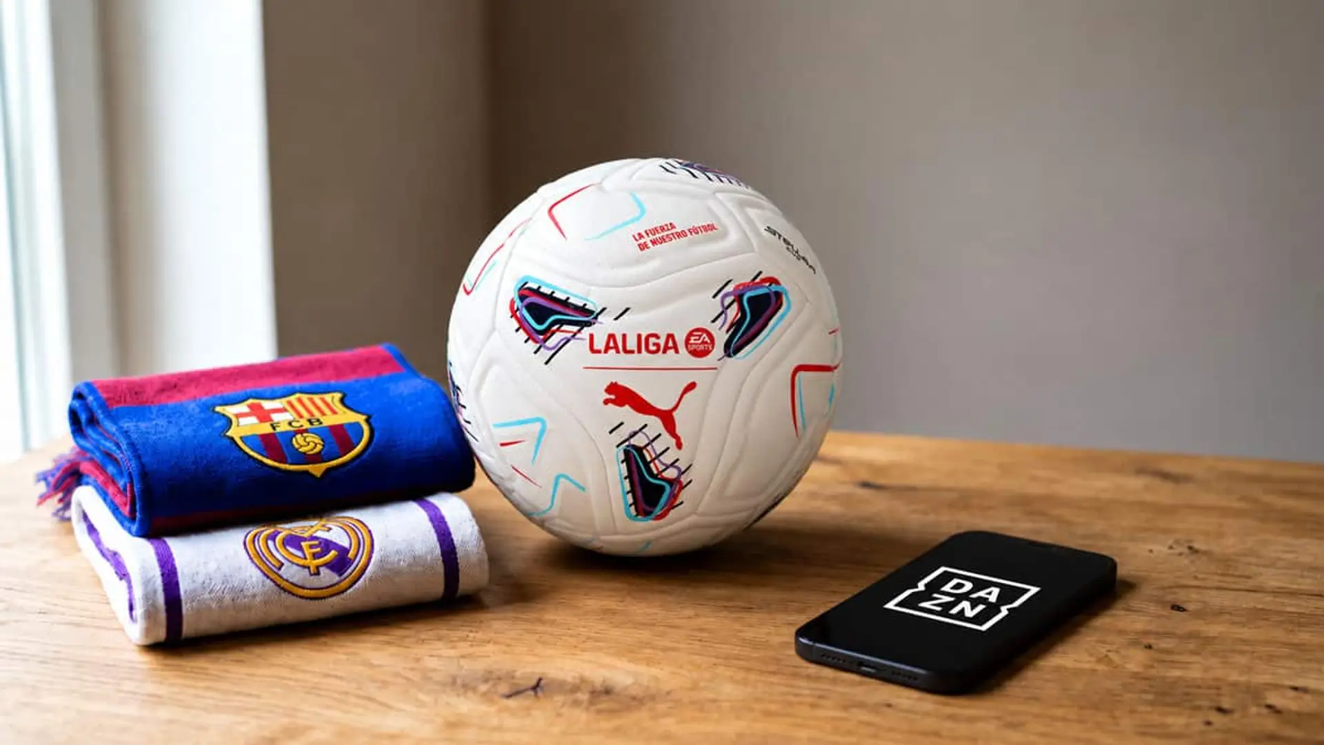 DAZN baja un 50% el Plan Fútbol por el Clásico: 9,99€ al mes si contratas hasta el 25 de octubre Balón oficial Puma de LaLiga junto a bufandas del FC Barcelona y Real Madrid y un móvil con el logotipo de DAZN.