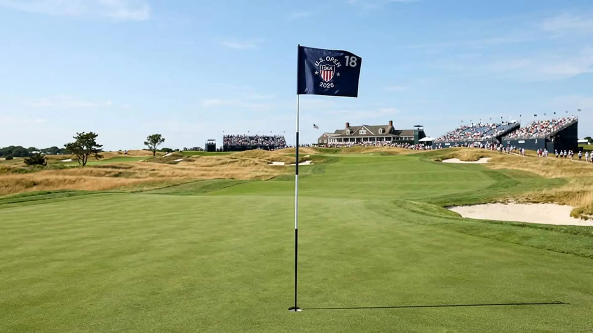 Bandera del US Open 2026 en el hoyo de un campo de golf con gradas y público al fondo