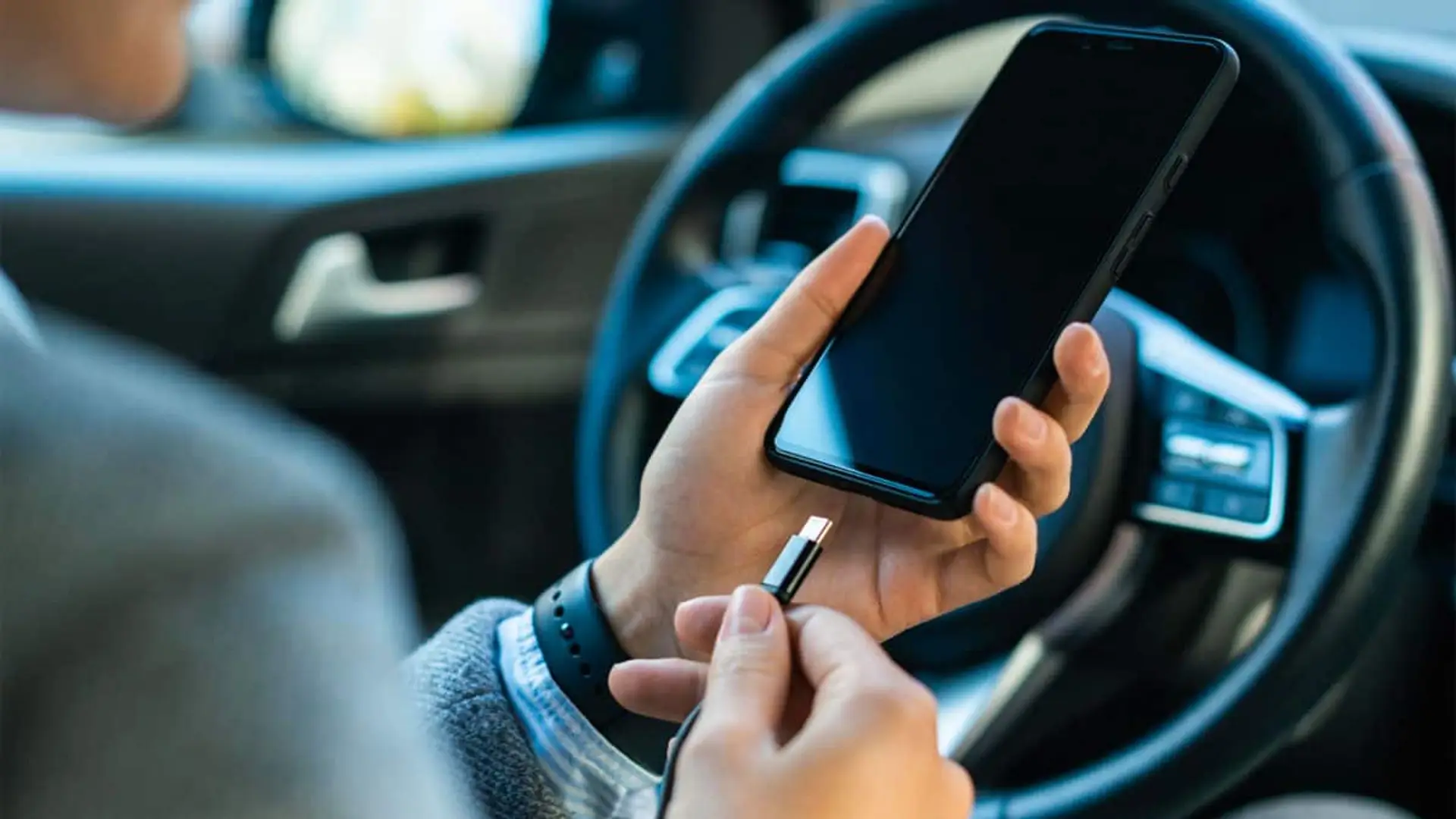Persona conectando un móvil a un cargador dentro de un coche.