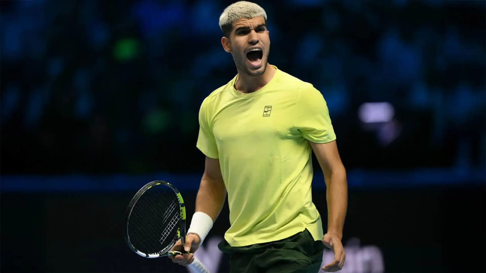 El tenista español Carlos Alcaraz celebrando un punto con intensidad durante un partido de tenis de las ATP Finals. Viste camiseta amarilla.