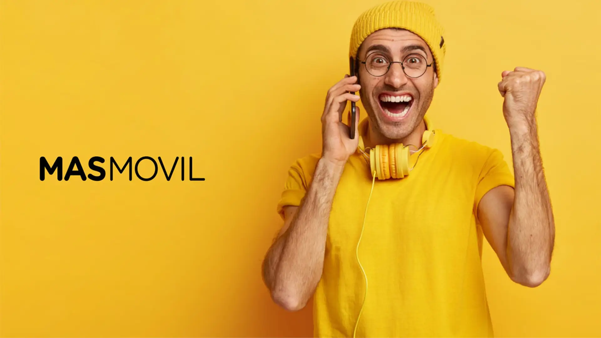 Joven celebrando una buena oferta de MásMóvil mientras habla por su smartphone sobre un fondo amarillo.
