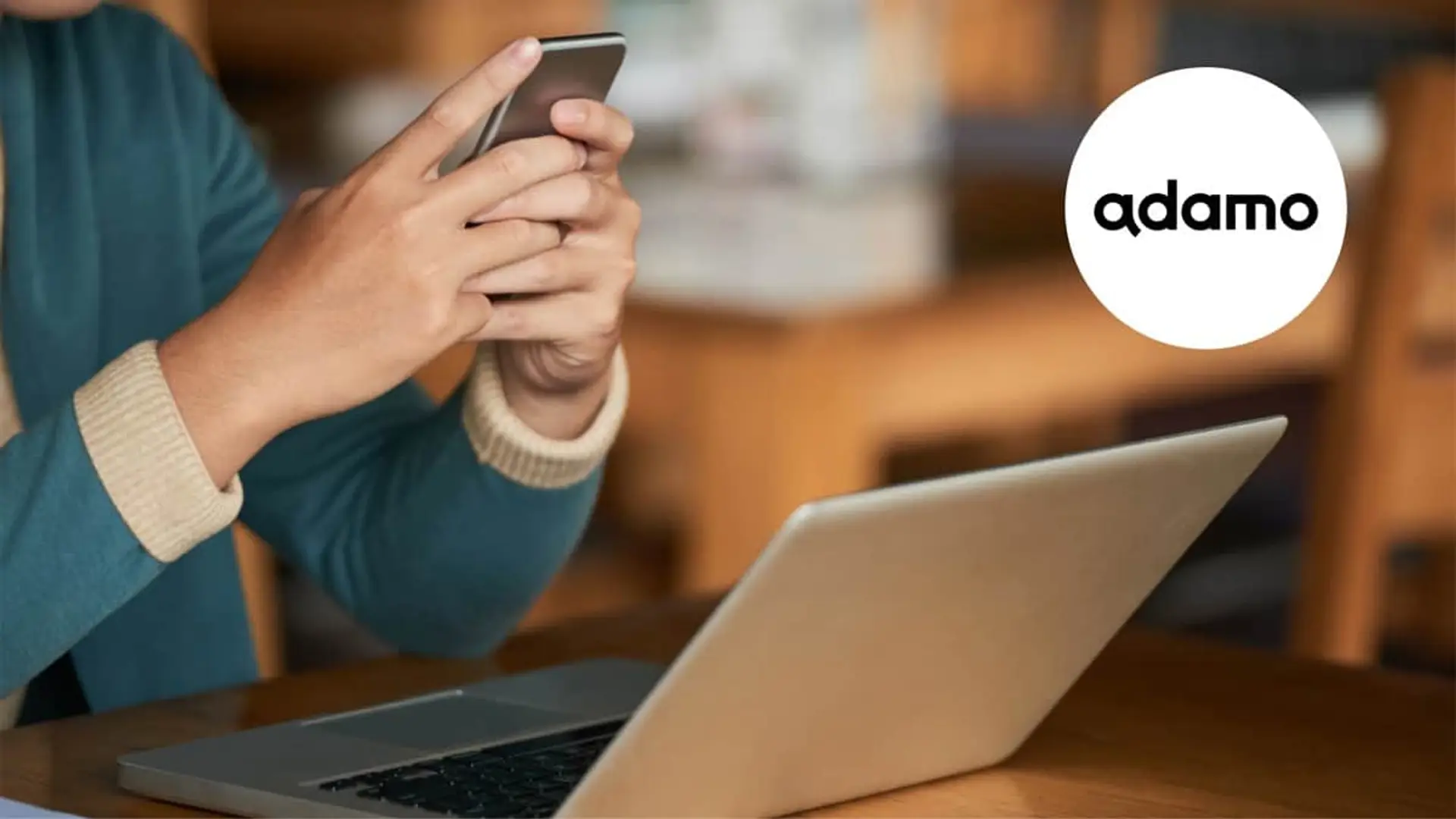Usuario con portátil y móvil junto al logotipo de Adamo para representar la conectividad de fibra y telefonía.