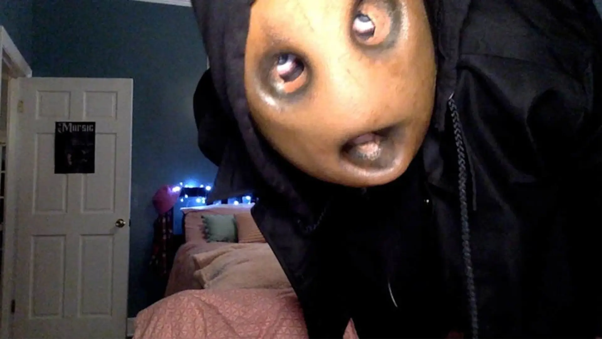 Una persona con una máscara de terror distorsionada se inclina hacia la cámara en un dormitorio, creando una escena inquietante.