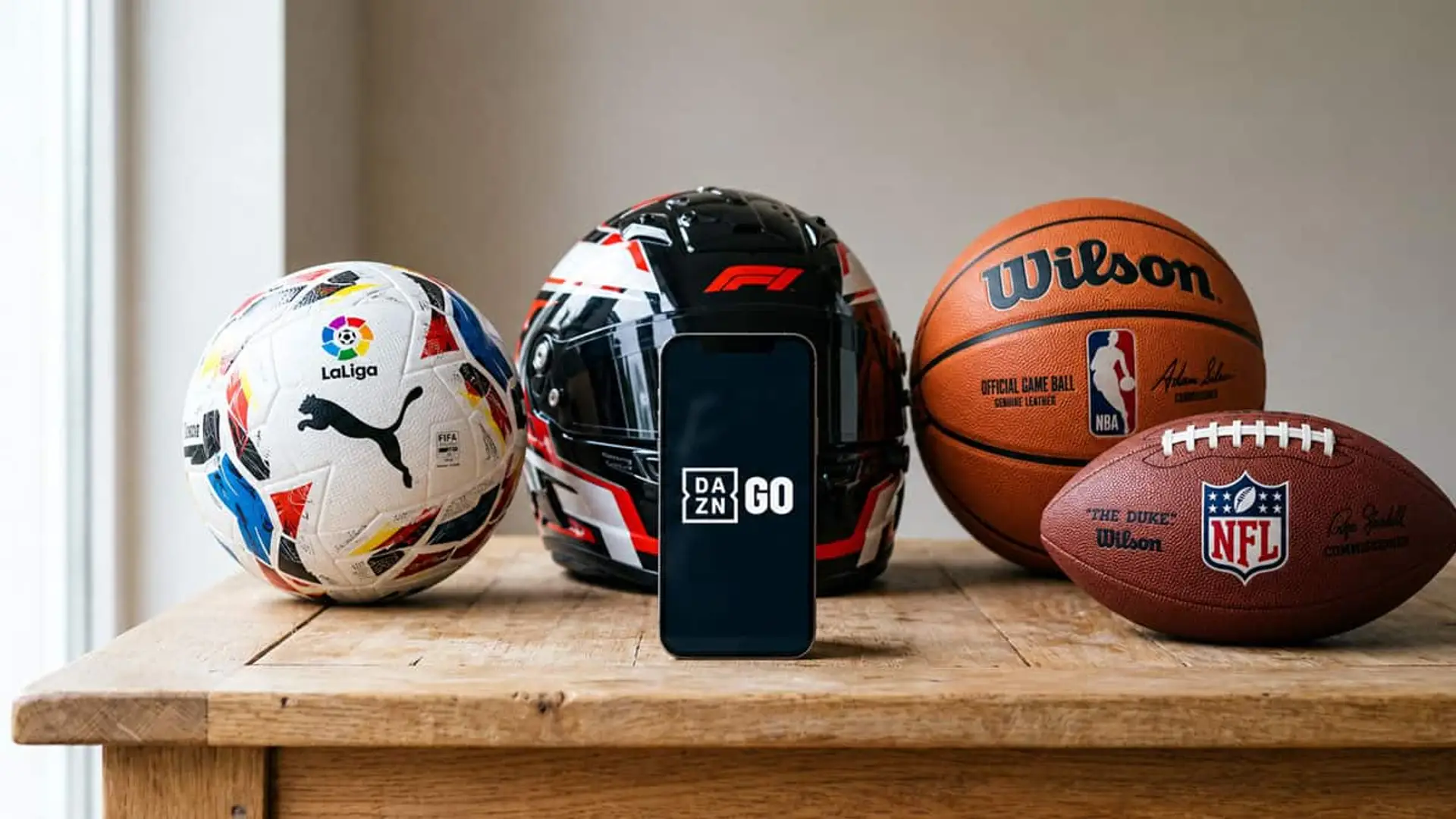 Móvil con el logotipo de DAZN GO junto a un balón de LaLiga, un casco de Fórmula 1 y balones oficiales de la NBA y la NFL.