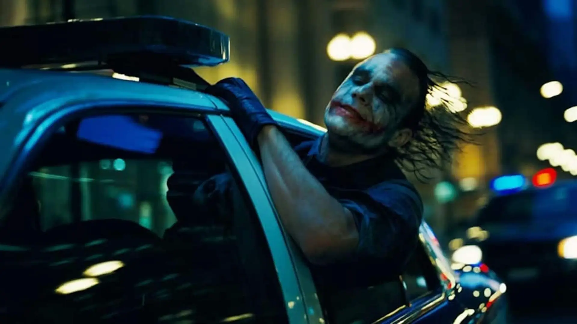 Escena de El caballero oscuro en la que el Joker recorre las calles sacando la cabeza del coche de policía.