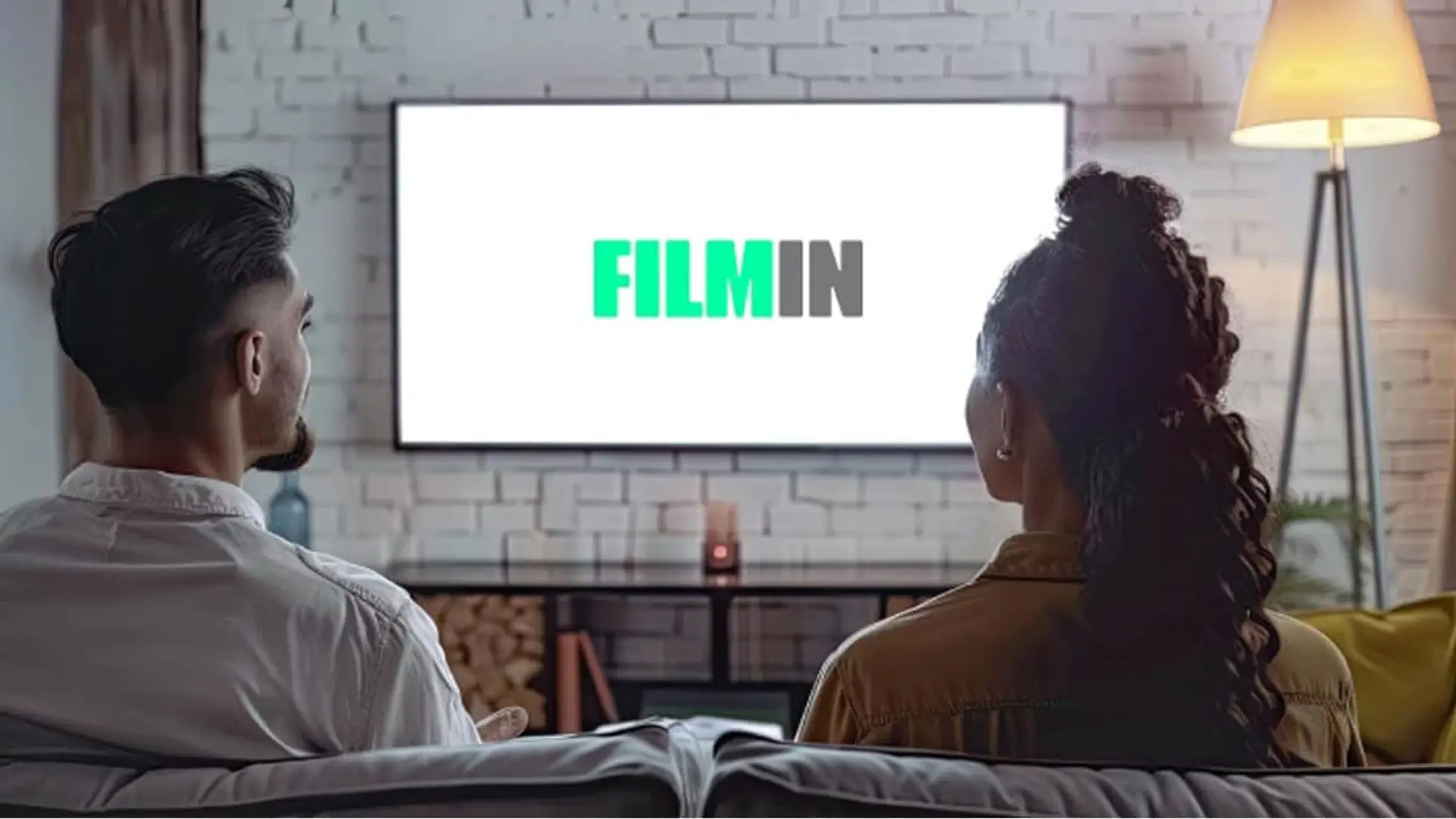 Pareja sentada en el sofá viendo la plataforma de cine y series Filmin en la televisión.