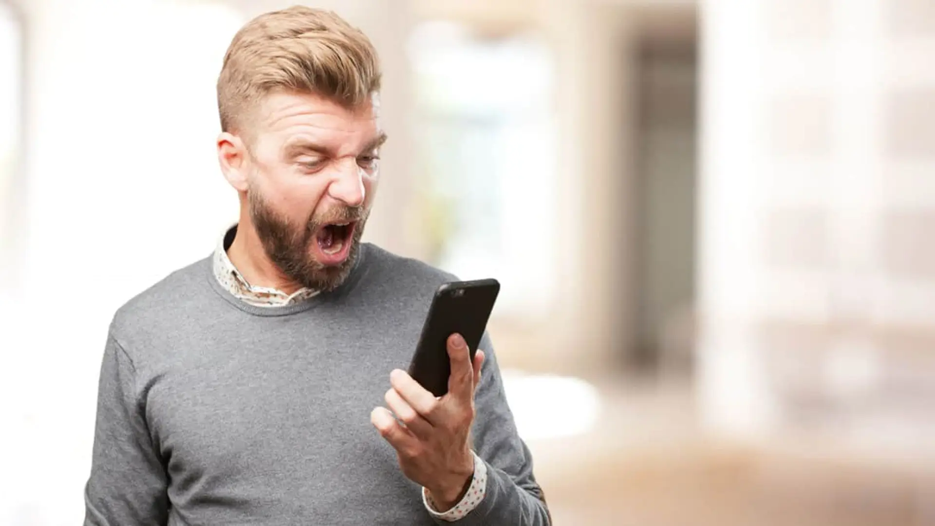 Caída de PTV Telecom: usuarios reportan incidencias en Sevilla y Málaga Hombre con barba enfadado gritando a su smartphone. Cliente frustrado por una mala experiencia en el servicio de telefonía.