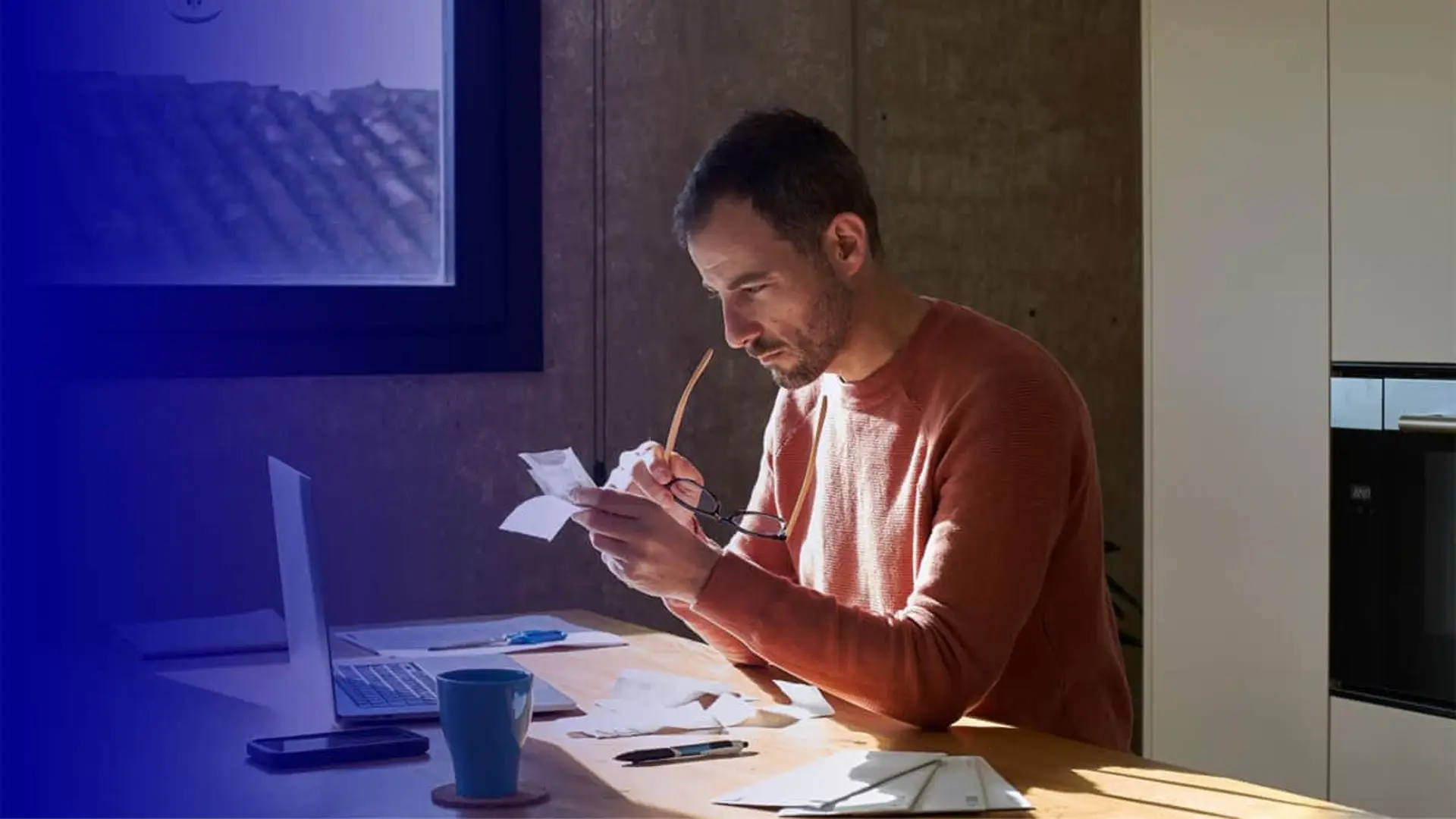 Hombre revisando facturas con un portátil en casa para gestionar su ahorro y economía doméstica.