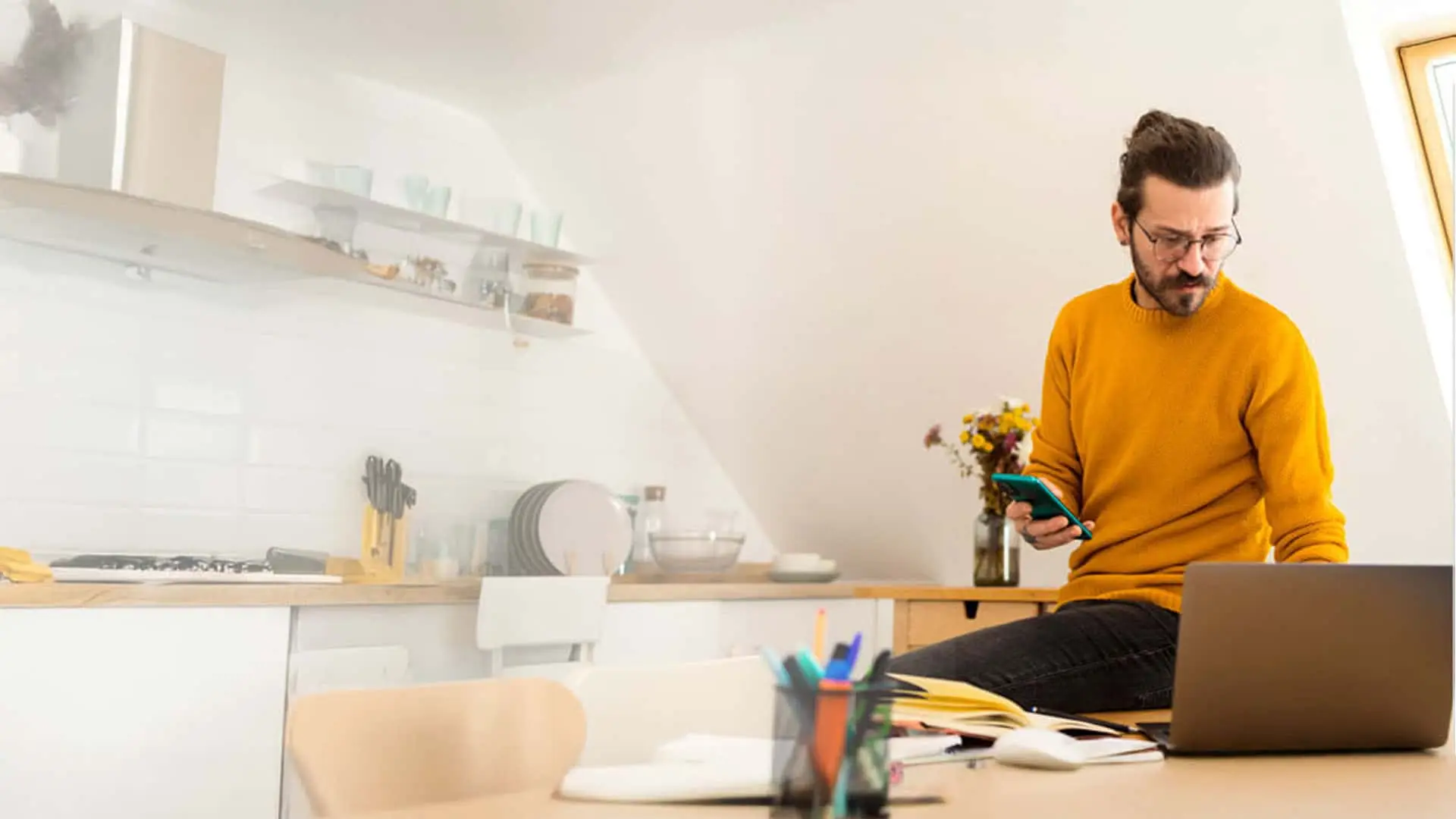 Autónomo trabajando desde casa, gestionando su negocio con el móvil y el portátil. Teletrabajo y flexibilidad laboral.