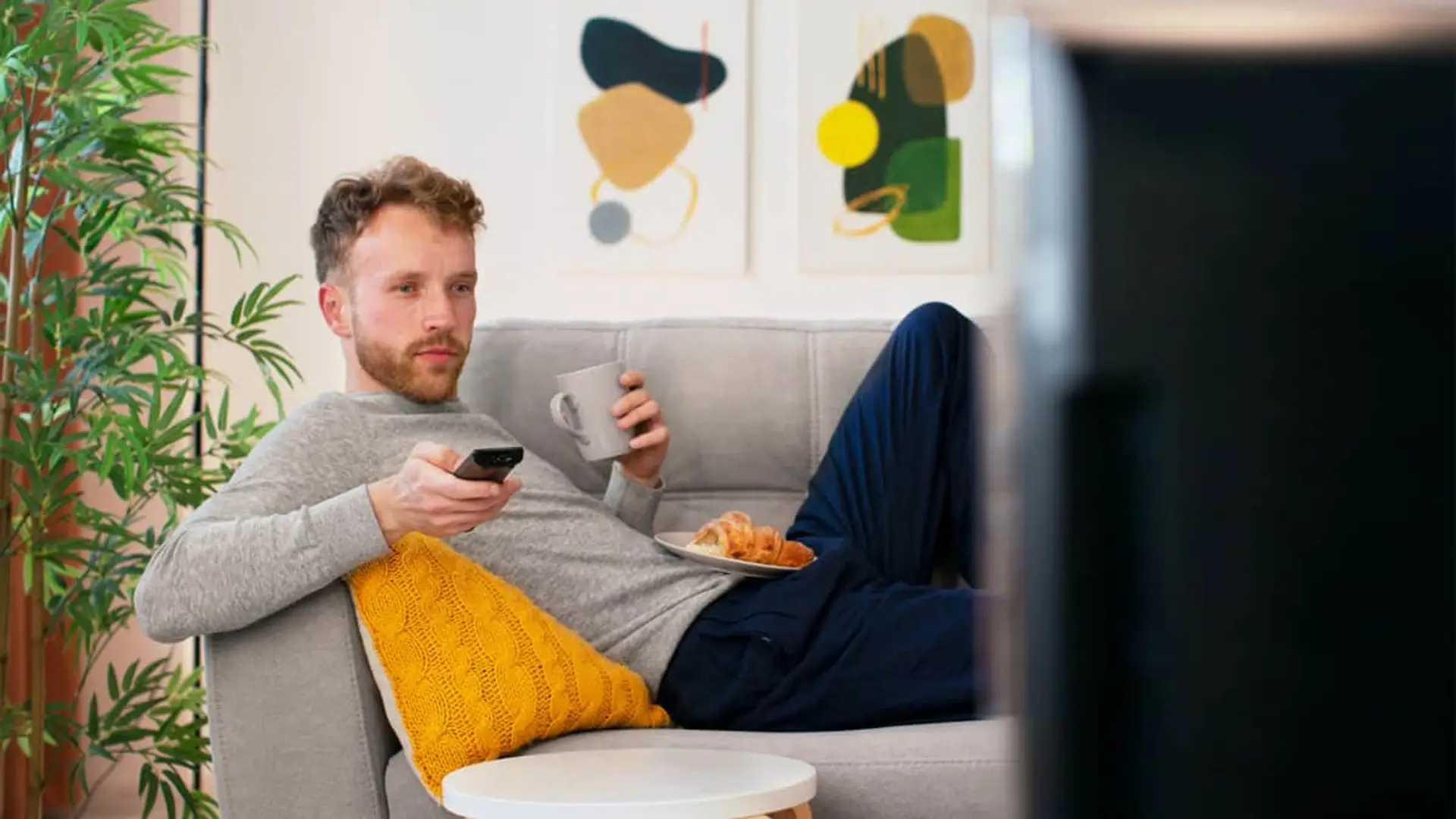Hombre relajado en el sofá viendo la televisión y usando el mando a distancia en un salón acogedor.