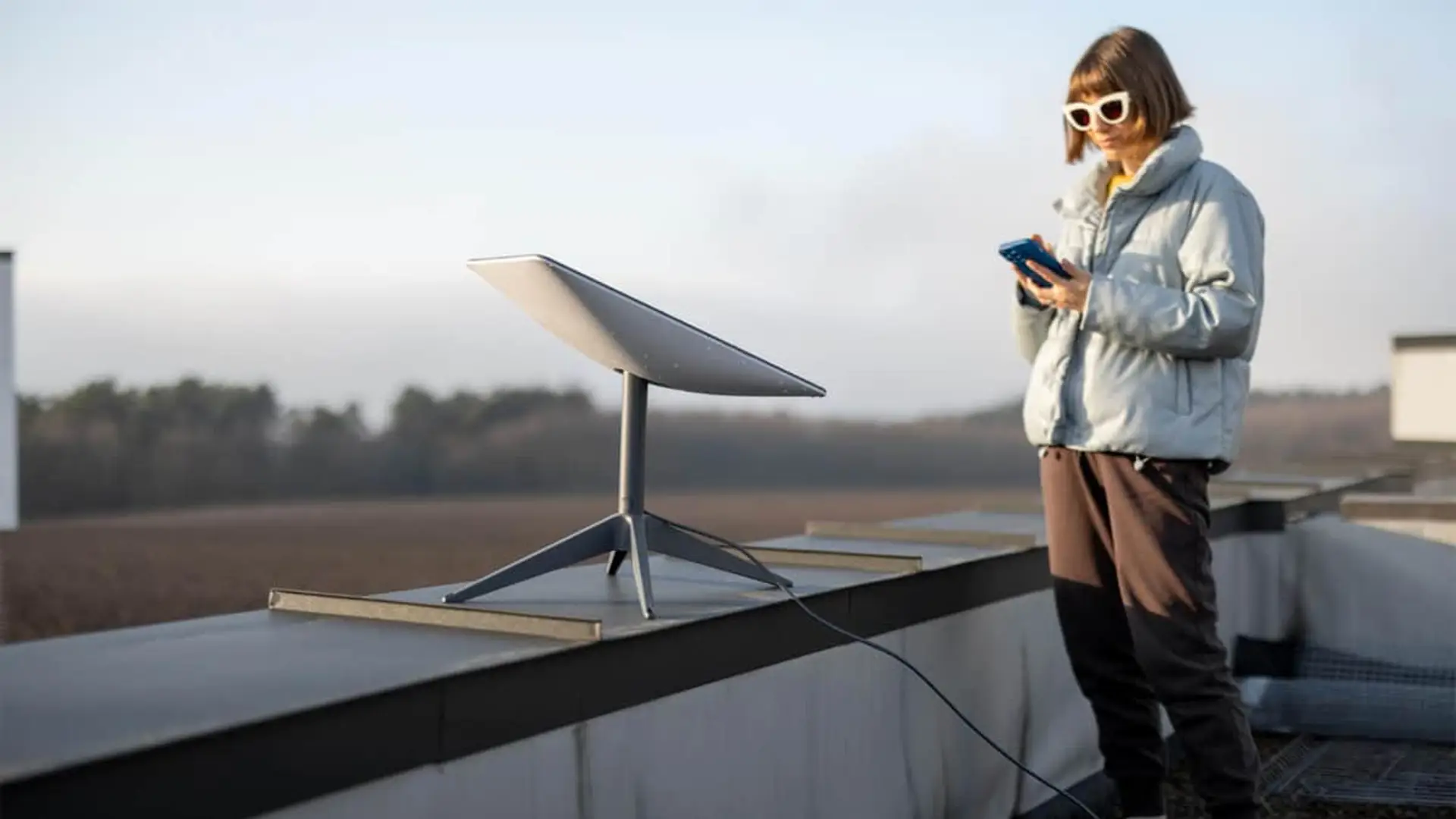 Mujer configurando una antena de Starlink desde su móvil en la terraza para obtener internet de alta velocidad en casa.
