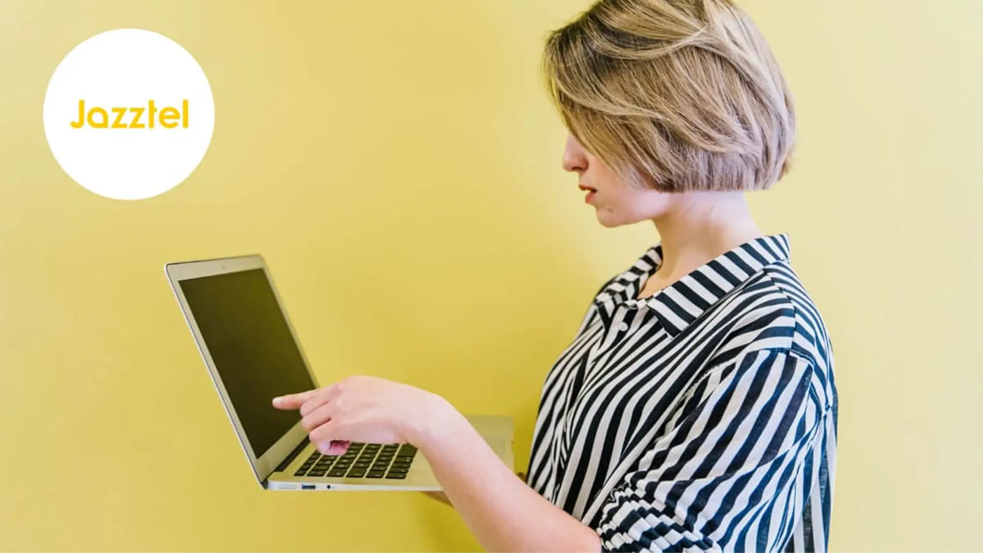 Jazztel elimina su fibra barata de 300Mb y fuerza el paso a una tarifa más cara (te guste o no) Mujer señalando un ordenador portátil junto al logo de Jazztel para contratar servicios de internet y fibra óptica.