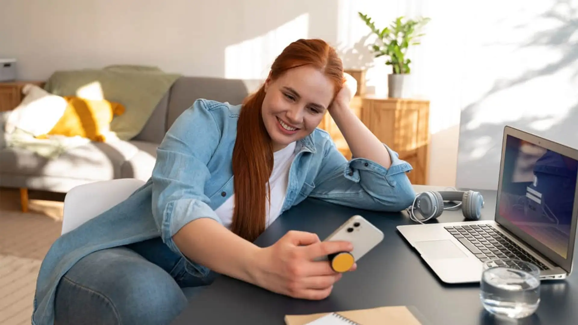 El precio de las tarifas de fibra baja en octubre y el móvil se congela: así queda cada operador Mujer sonriente usando su móvil y portátil para acceder a servicios online o a su banca digital desde casa.