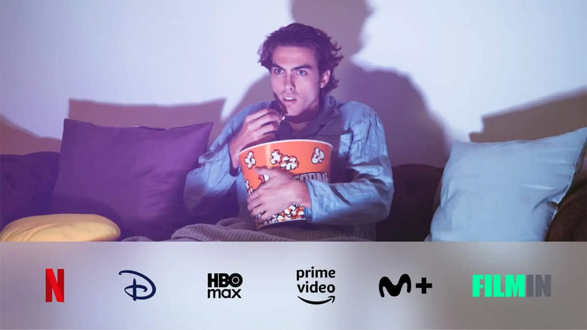 Joven sorprendido viendo una película de miedo en el sofá con un cuenco de palomitas y logos de plataformas de streaming.