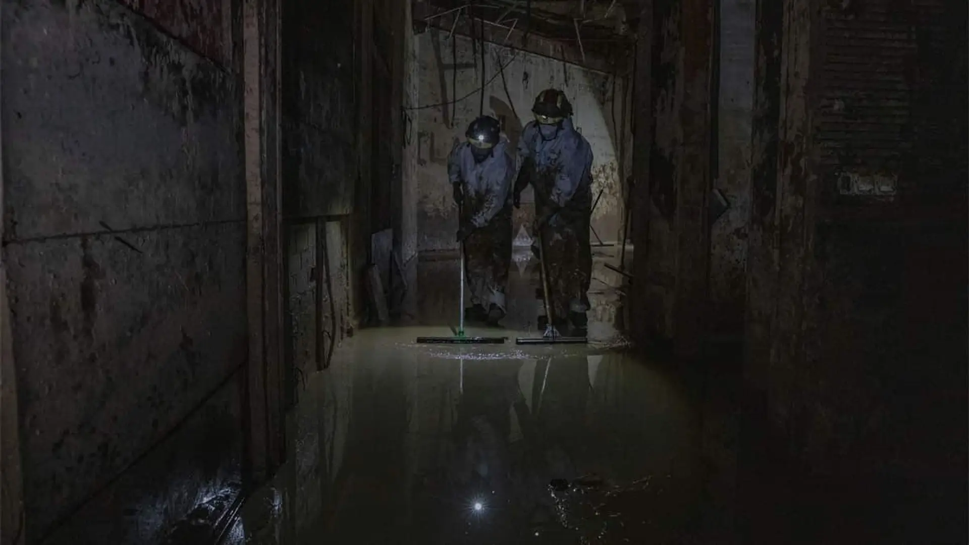 Equipo de emergencias limpiando agua y barro en el interior de un edificio afectado por inundaciones de la dana de 2024.