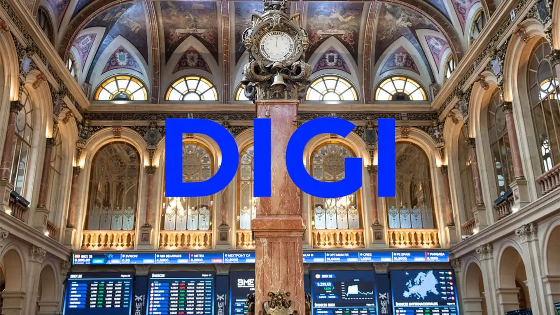 Logo de Digi sobre el interior de la Bolsa de Madrid, con paneles de cotización al fondo.