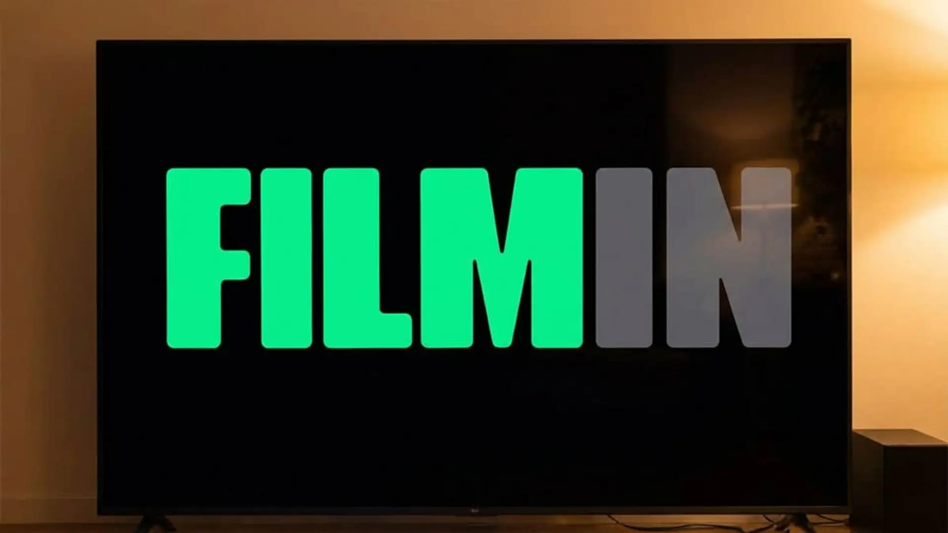 Logotipo verde y gris de Filmin en pantalla de televisor en salón a oscuras.