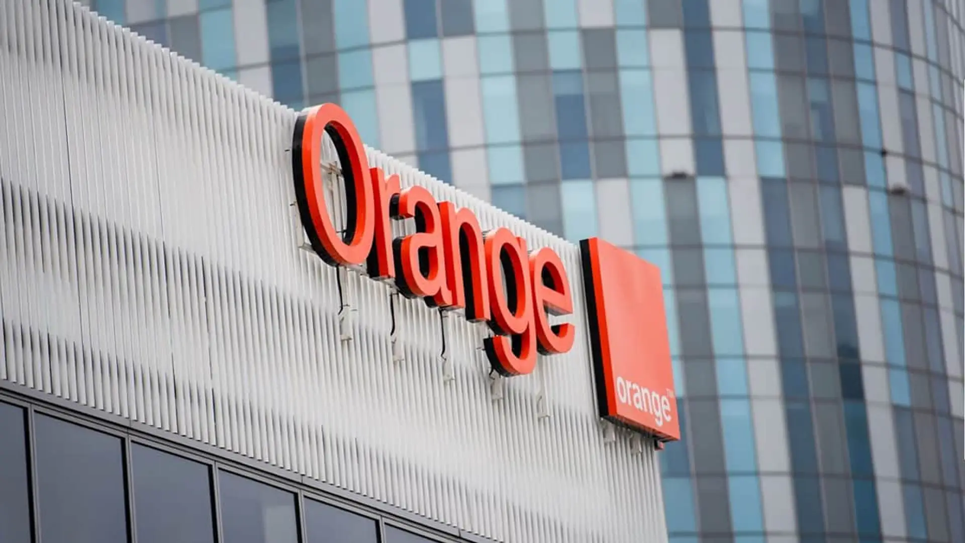 Logotipo de Orange en la fachada de un edificio corporativo moderno para servicios de fibra óptica y móvil.