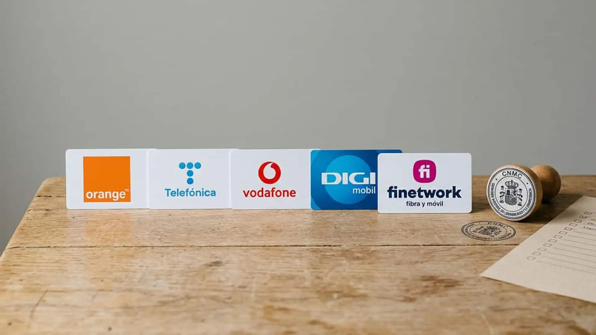 Logos de Orange, Telefónica, Vodafone, DIGI y Finetwork junto a un sello de la CNMC sobre una mesa de madera.