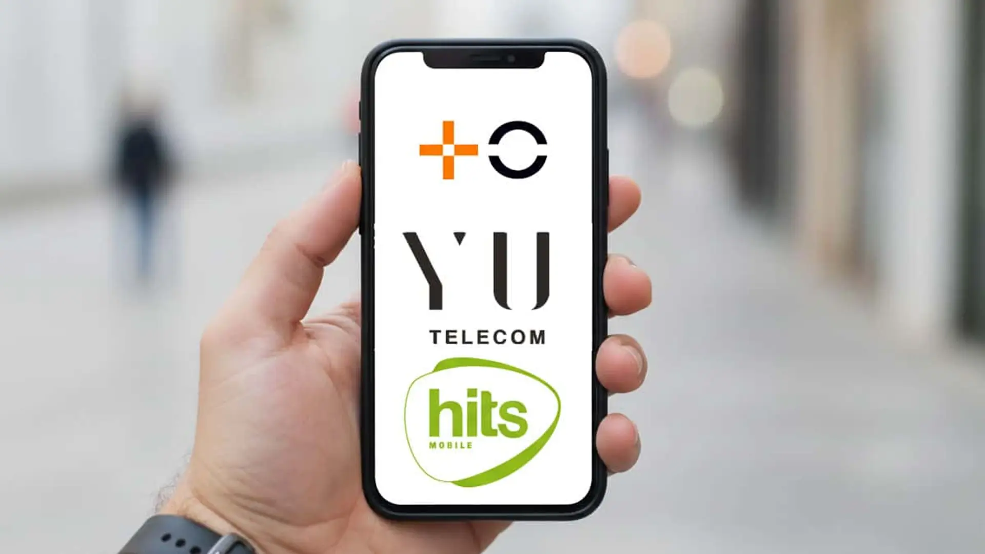 Conflicto MasOrange, Yu Telecom y Hits Mobile: así quedan sus clientes Mano sosteniendo un teléfono móvil que muestra los logotipos de MasOrange, Yu Telecom y Hits Mobile en la pantalla.