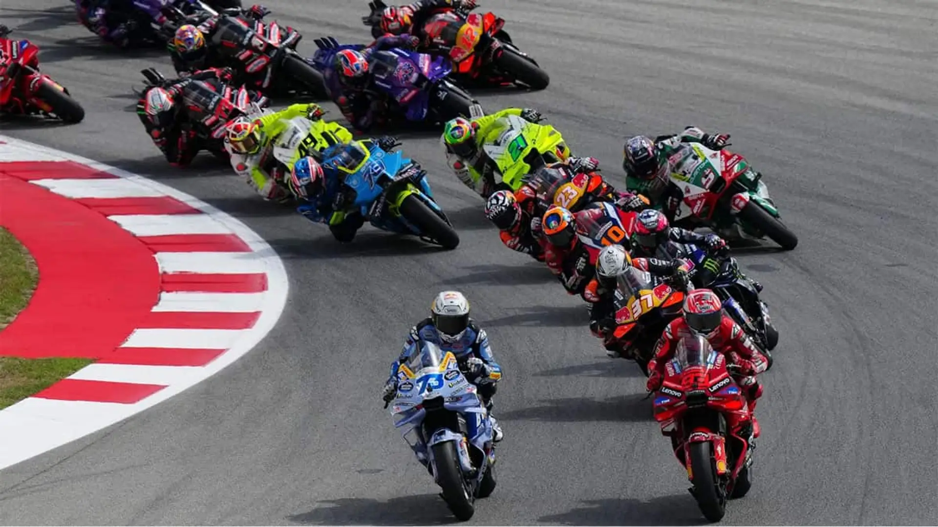 Grupo de pilotos de MotoGP tomando una curva en plena carrera, con motos de distintas escuderías compitiendo por la primera posición.