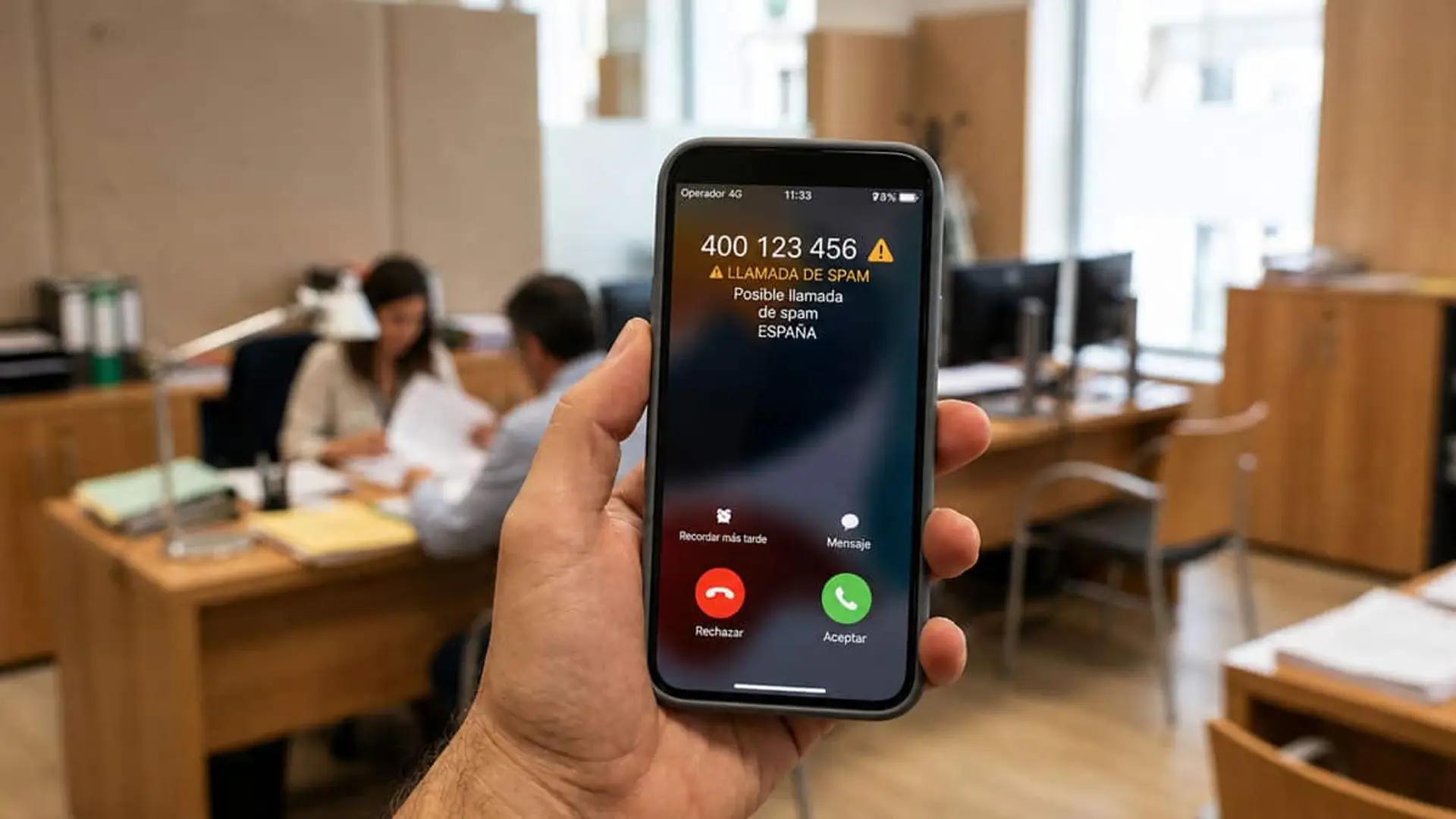 Llega el prefijo 400 contra las llamadas comerciales: así las identificarás y podrás bloquearlas Mano sujetando un móvil con una alerta de posible llamada de spam en una oficina con varias personas al fondo