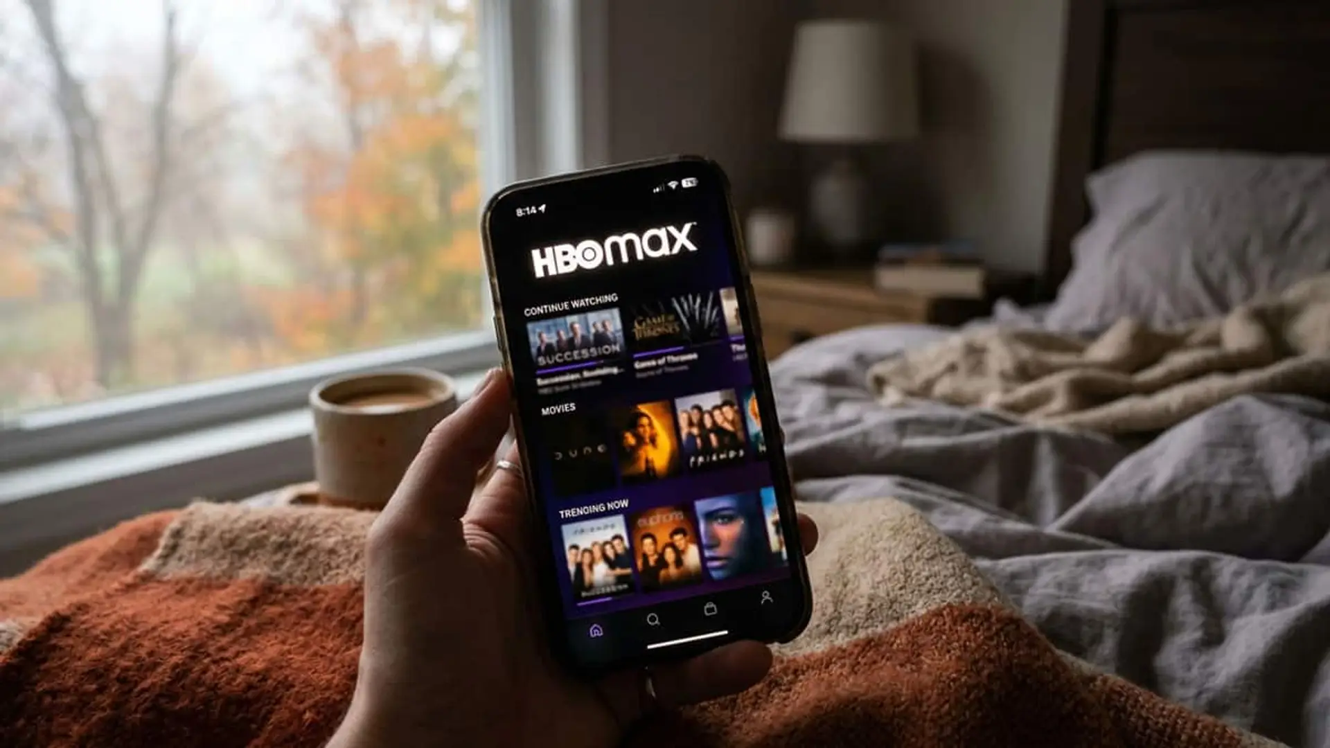 Mano sujetando un móvil con la app de HBO Max abierta sobre una cama