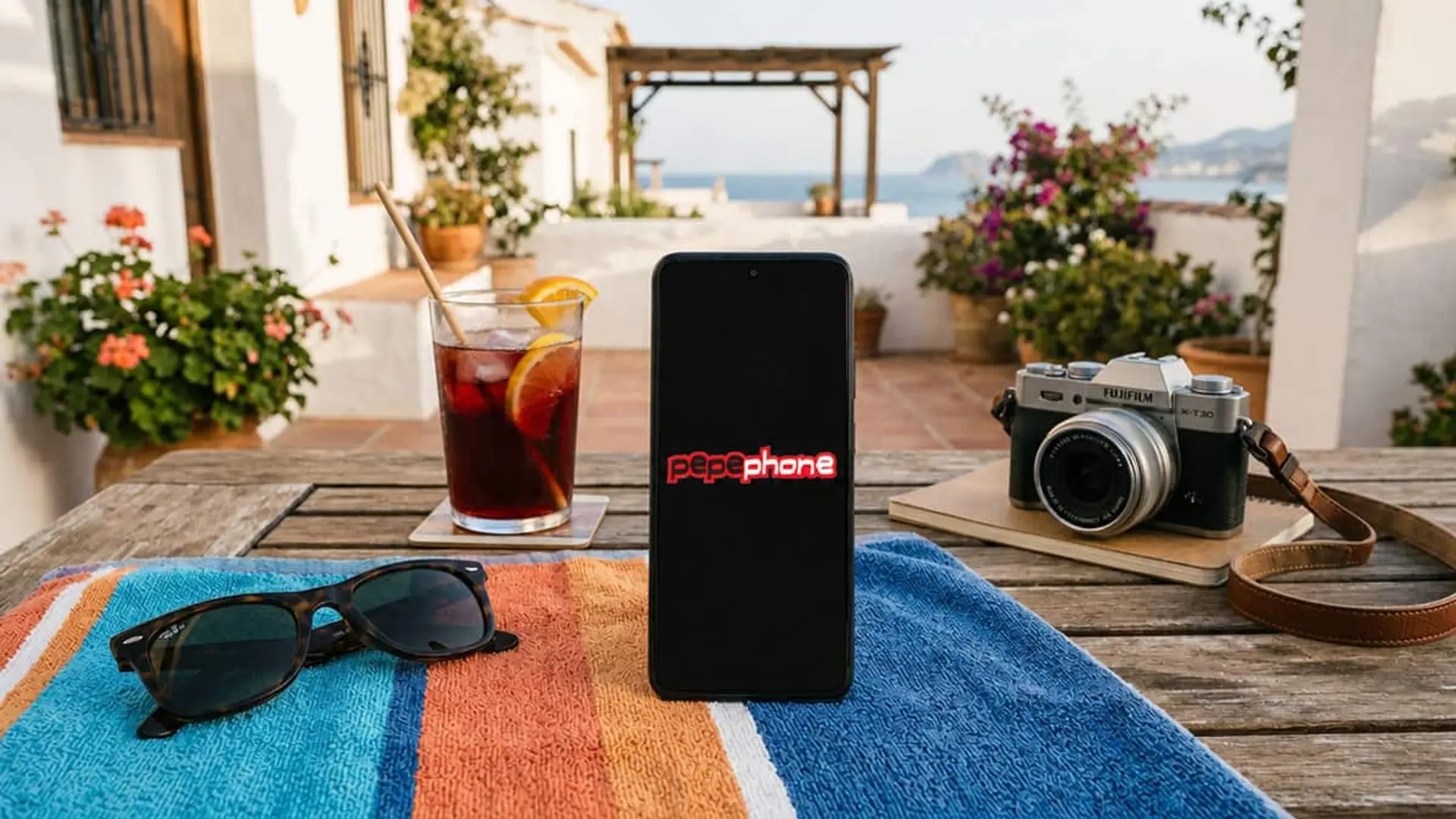 Pepephone encadena su tercera subida de gigas en un mes: la tarifa de 15 euros ya tiene 150 GB Teléfono móvil con el logo de Pepephone sobre una mesa junto a unas gafas de sol, una cámara y una bebida