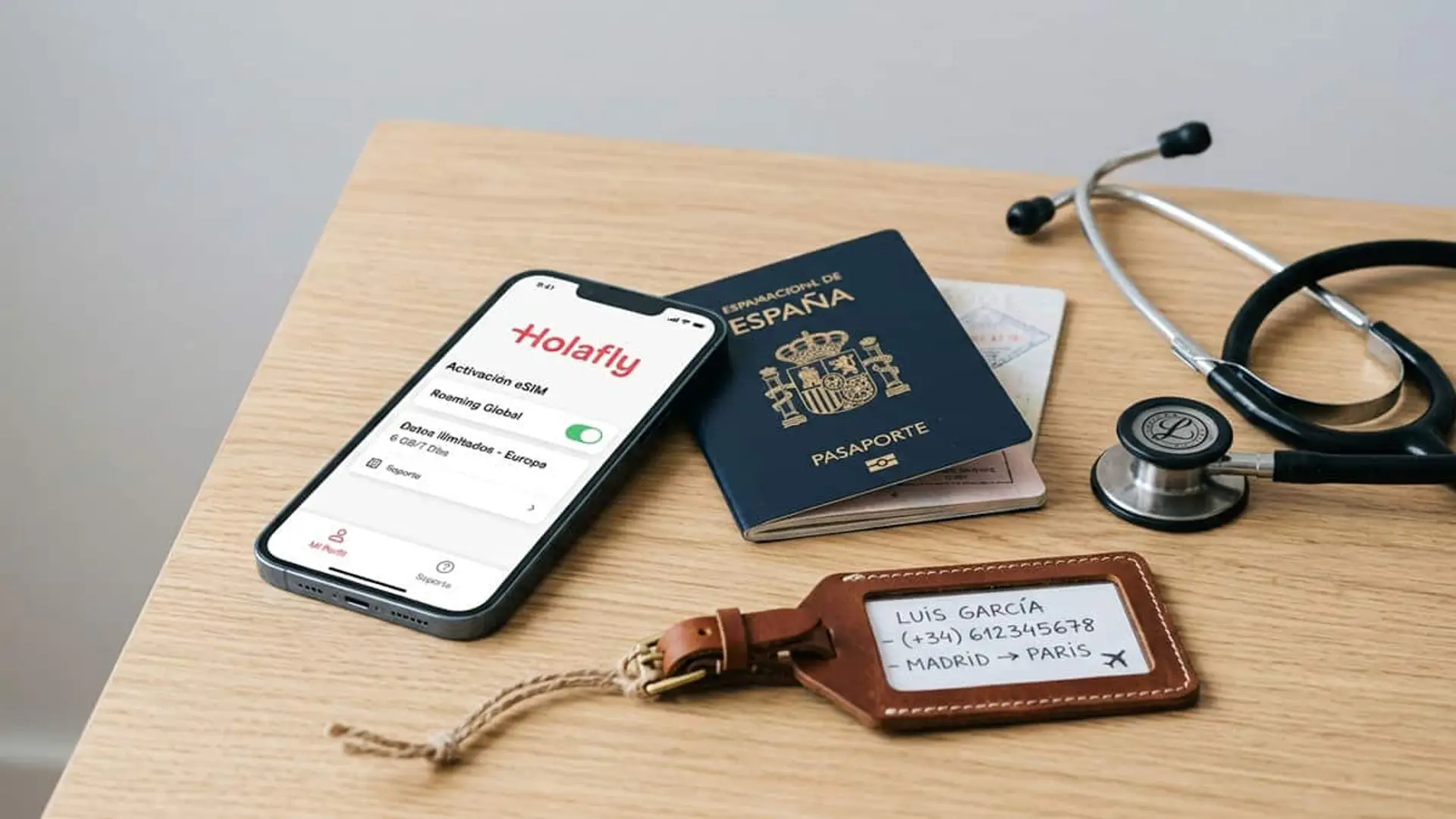 Teléfono móvil con la aplicación de Holafly y una eSIM activada, junto a un pasaporte español, un fonendoscopio y una etiqueta de equipaje sobre una mesa de madera.