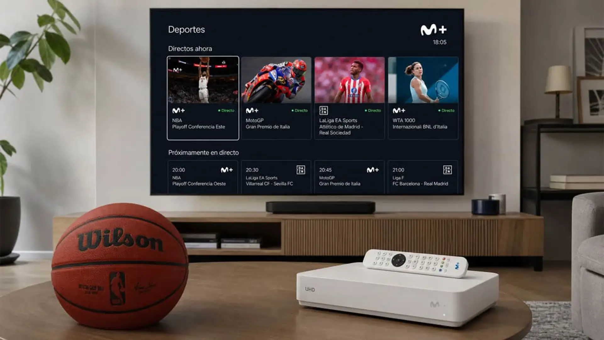 Descodificador Movistar+ UHD con mando frente a TV con sección Deportes en directo, junto a un balón de baloncesto Wilson NBA