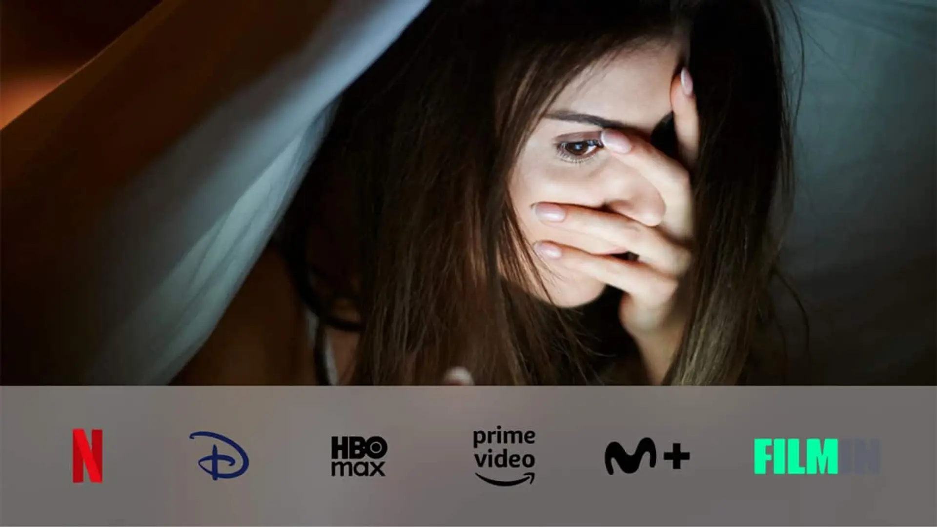 Joven asustada bajo una manta mientras ve una serie de miedo en casa, con logos de plataformas de streaming.