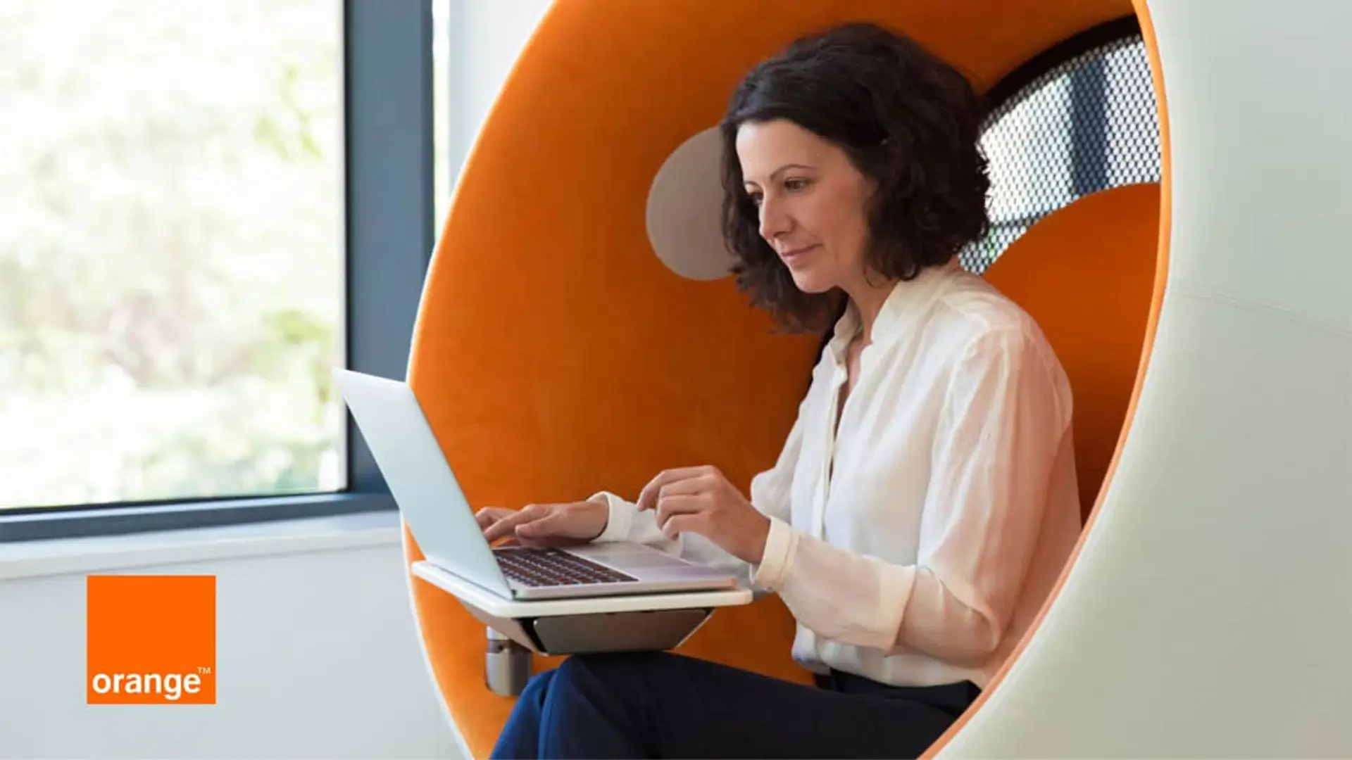 Orange despliega fibra óptica con una sola visita técnica en lugar de tres: el primer sistema así en Europa Mujer trabajando con su portátil con el logo de Orange para representar conexión a internet en la oficina.
