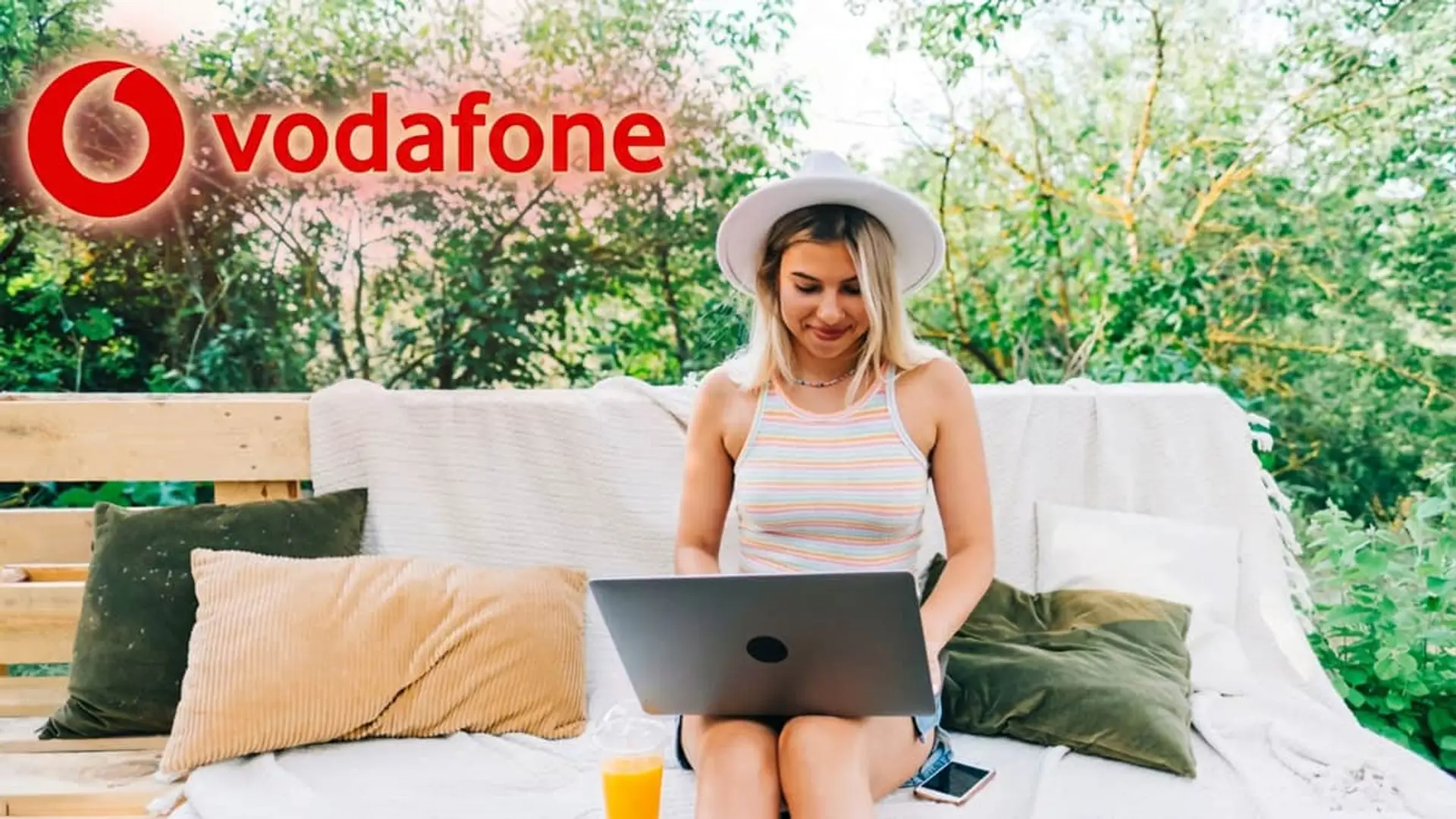 Mujer con un portátil en un jardín bajo el logo de Vodafone, representando la conexión a internet en exteriores.