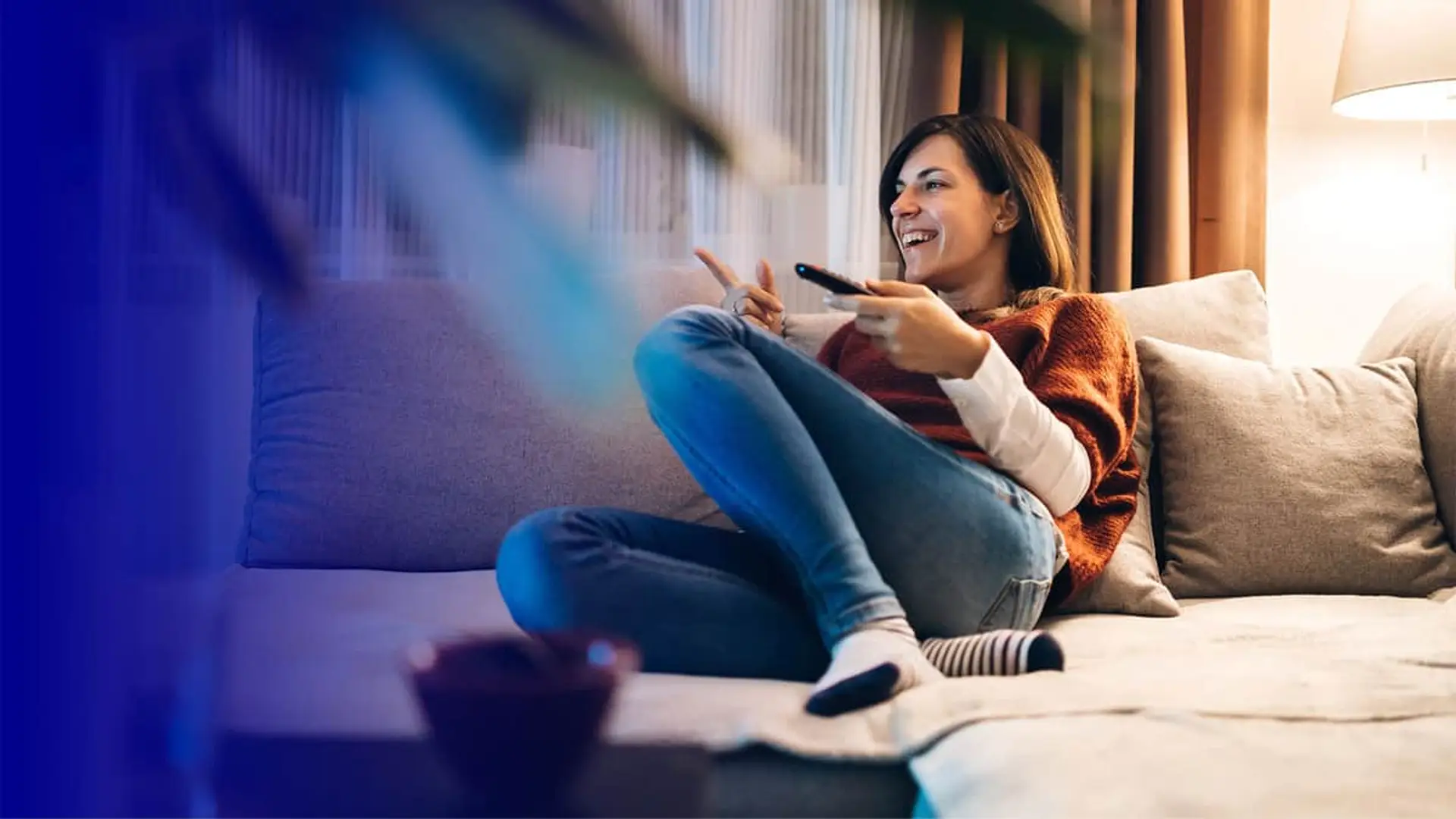 Mujer sonriente viendo televisión en el sofá con mando a distancia en ambiente acogedor