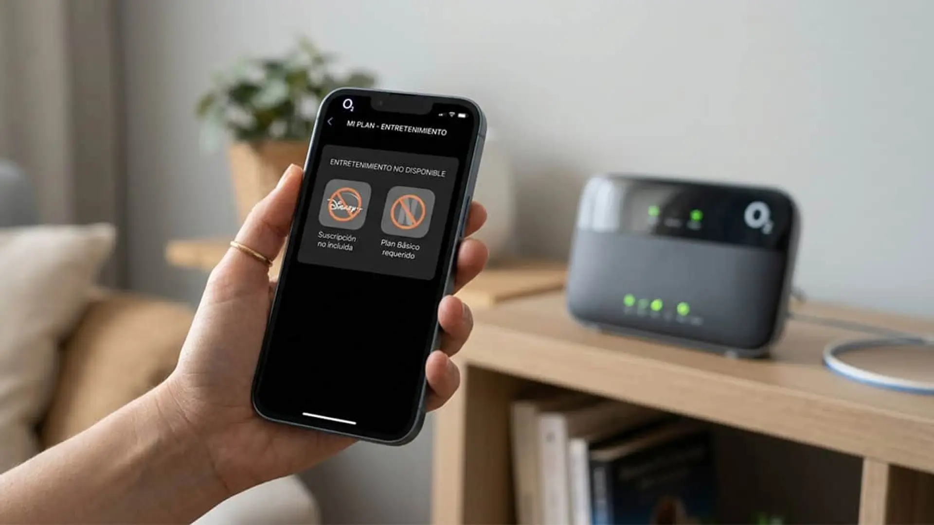 O2 mantiene Disney+, Netflix y Movistar Plus atados a la fibra pese a las peticiones de sus clientes Persona sosteniendo un teléfono móvil con la aplicación de O2 y un aviso de entretenimiento no disponible, junto a un router sobre un mueble