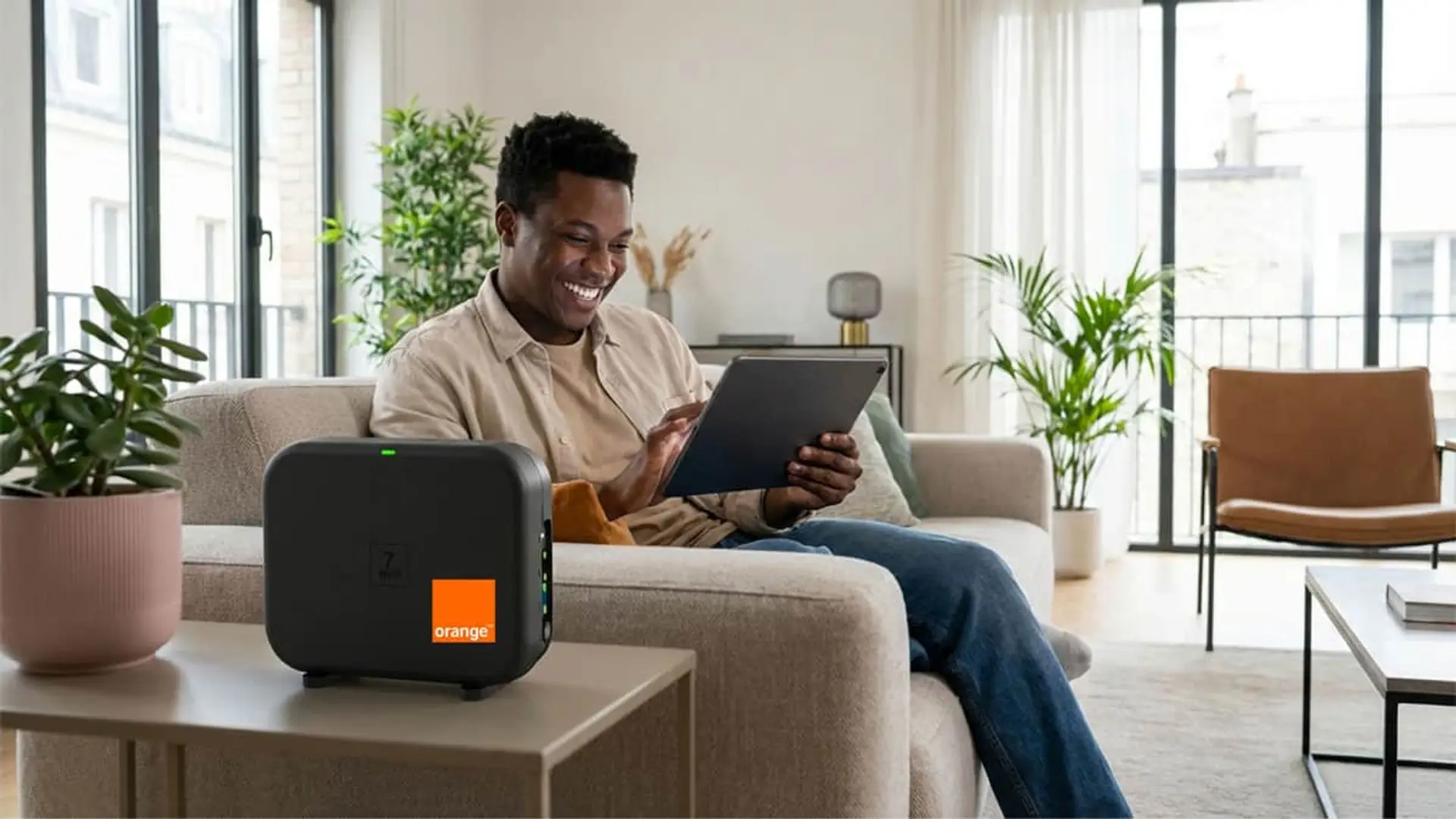 Hombre usando tablet junto a un repetidor Wi-Fi 7 de Orange en el salón para conexión de internet por fibra óptica en casa.