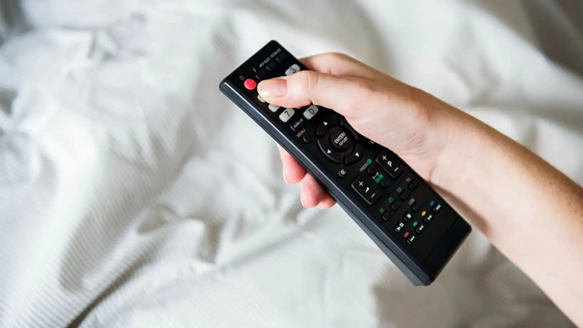 Un histórico canal se va de la TDT: dejará de emitir el 31 de diciembre de 2025 Persona usando un control remoto para cambiar de canal mientras está en la cama.