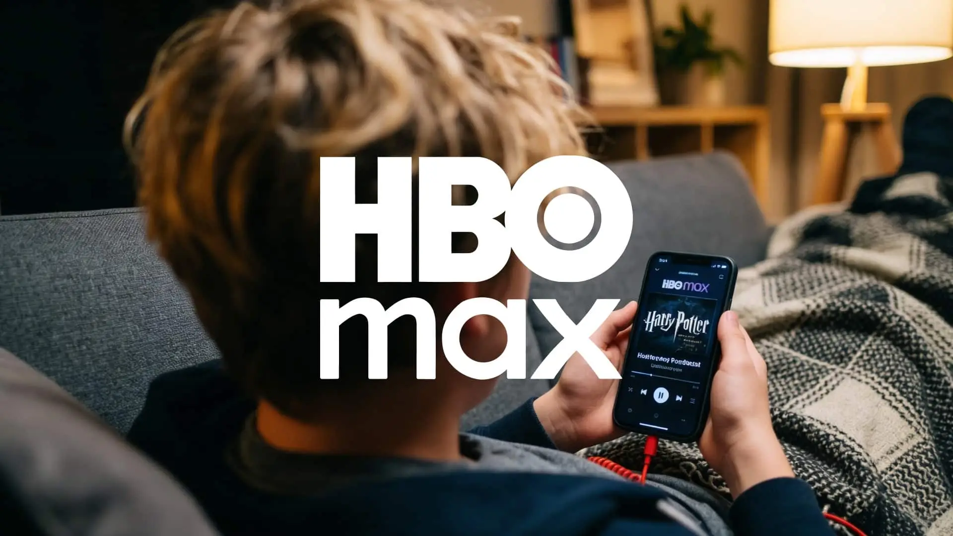 Persona usando HBO Max en el móvil mientras está tumbada en un sofá con una manta