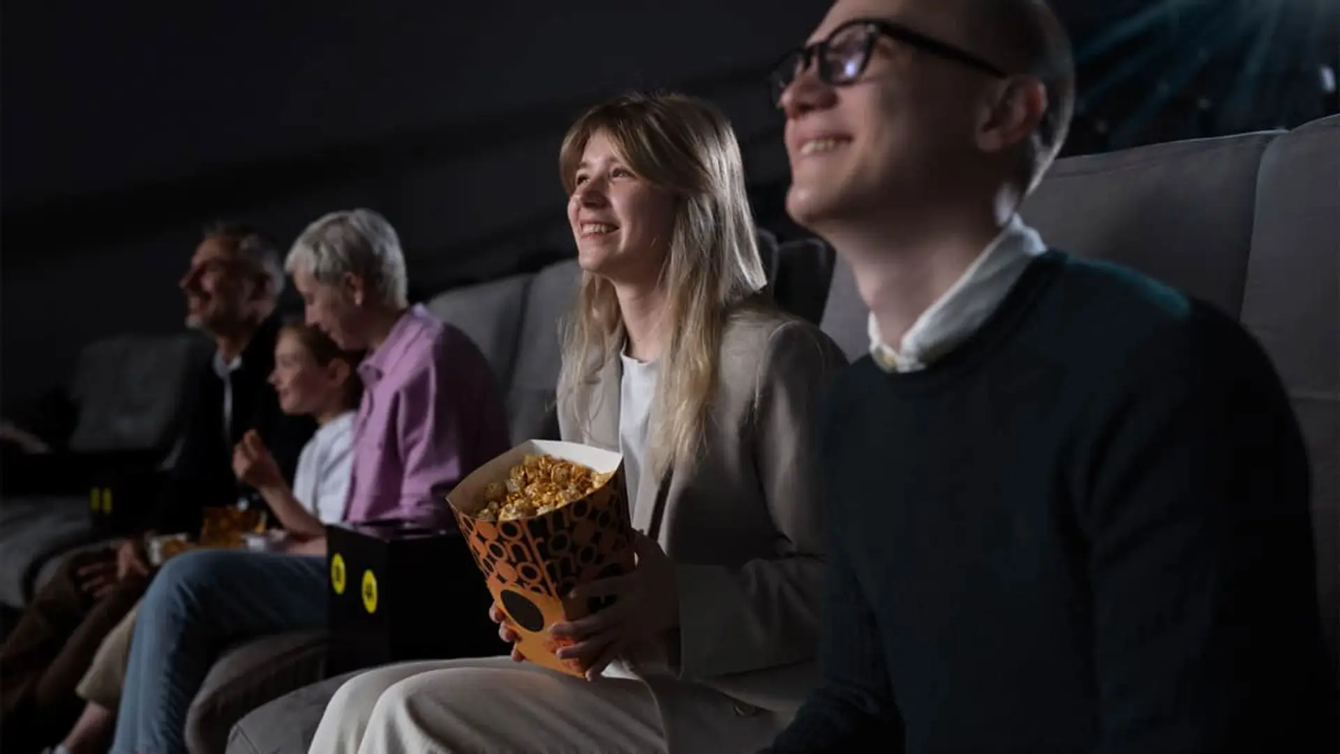 Qué ver en la Fiesta del Cine: 8 películas imprescindibles en cartelera para aprovechar las entradas baratas Espectadores en cine disfrutando una película en la Fiesta del Cine; mujer con palomitas sonríe en primera fila.