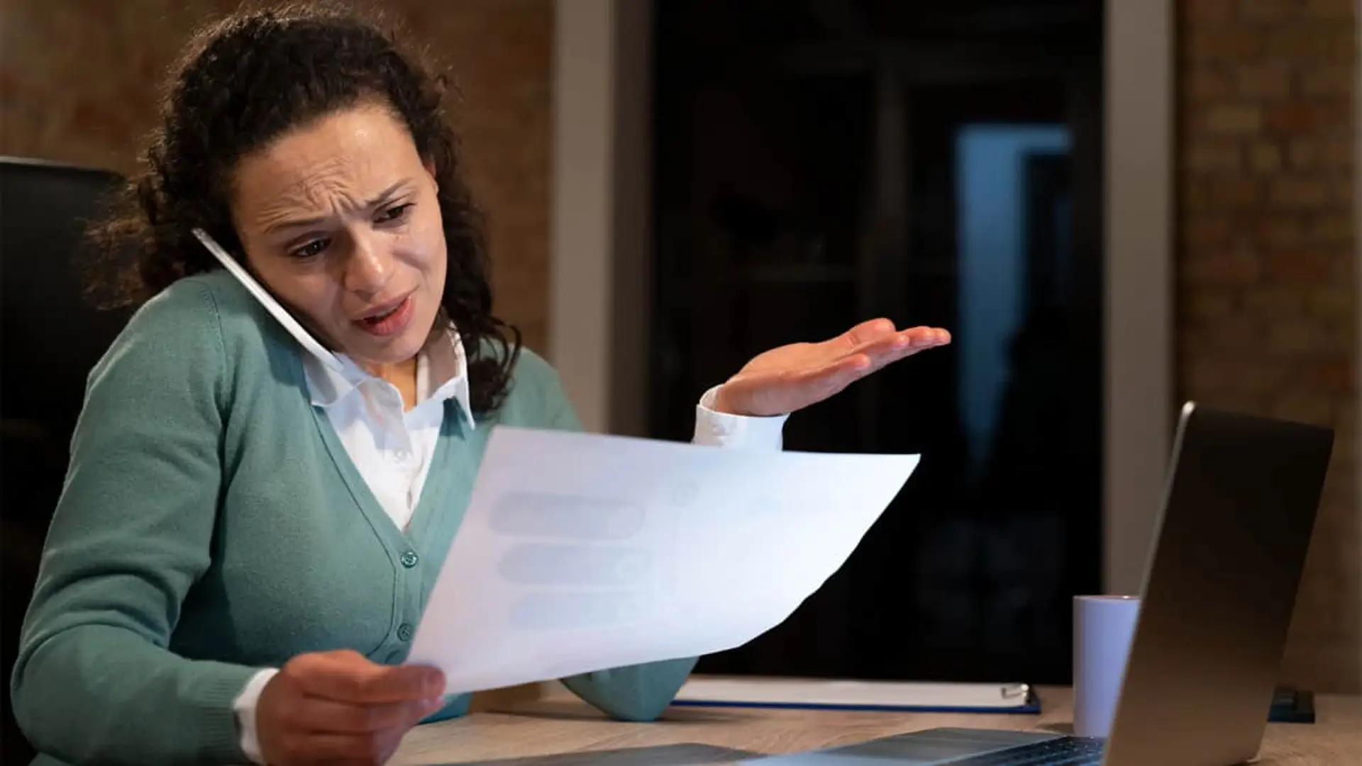 Cliente preocupada revisando factura elevada y reclamando por teléfono frente al ordenador