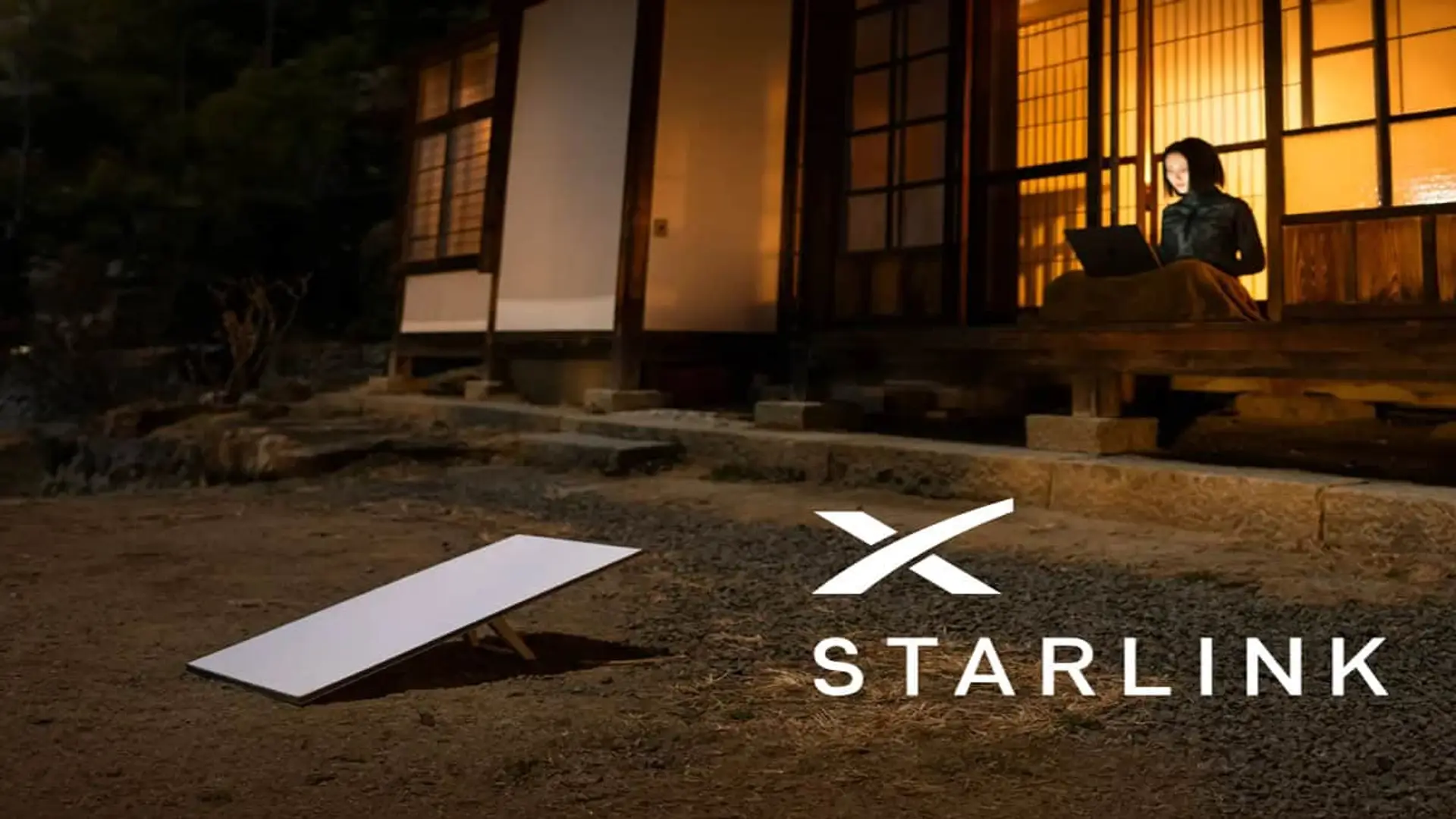 Antena de internet satelital Starlink en una zona rural con una mujer usando un portátil en casa por la noche.