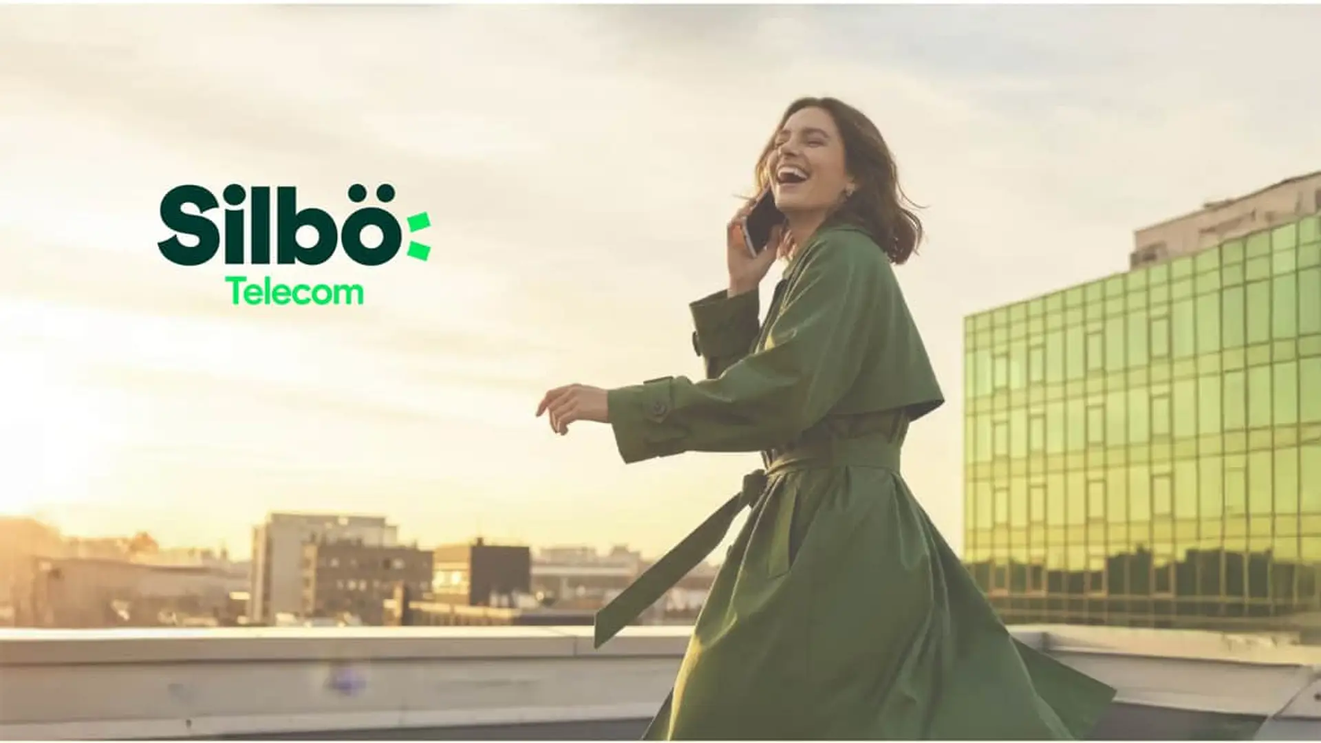 Mujer con abrigo verde hablando por teléfono en una terraza junto al logotipo de Silbö Telecom para red móvil.