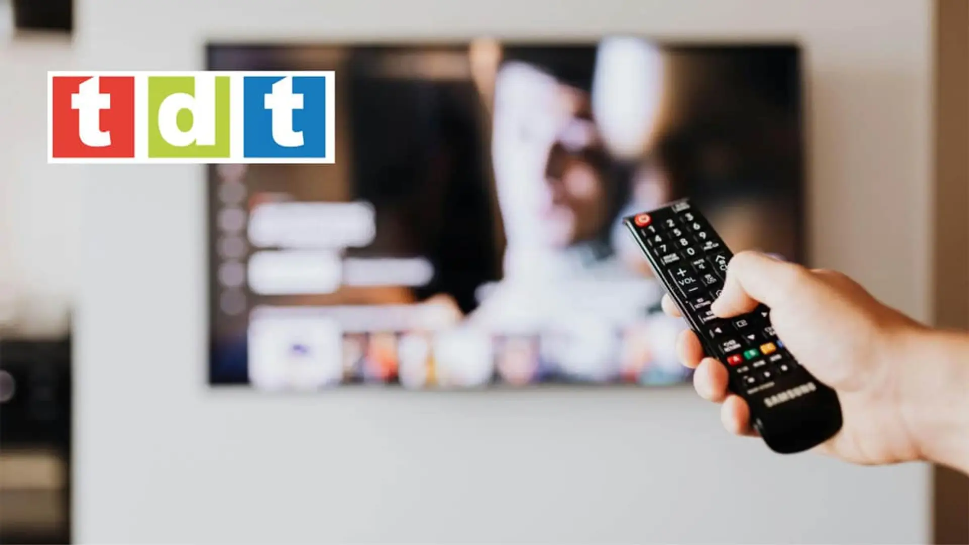 Mano con mando a distancia apuntando a un televisor con el logo de la TDT para sintonizar canales digitales.