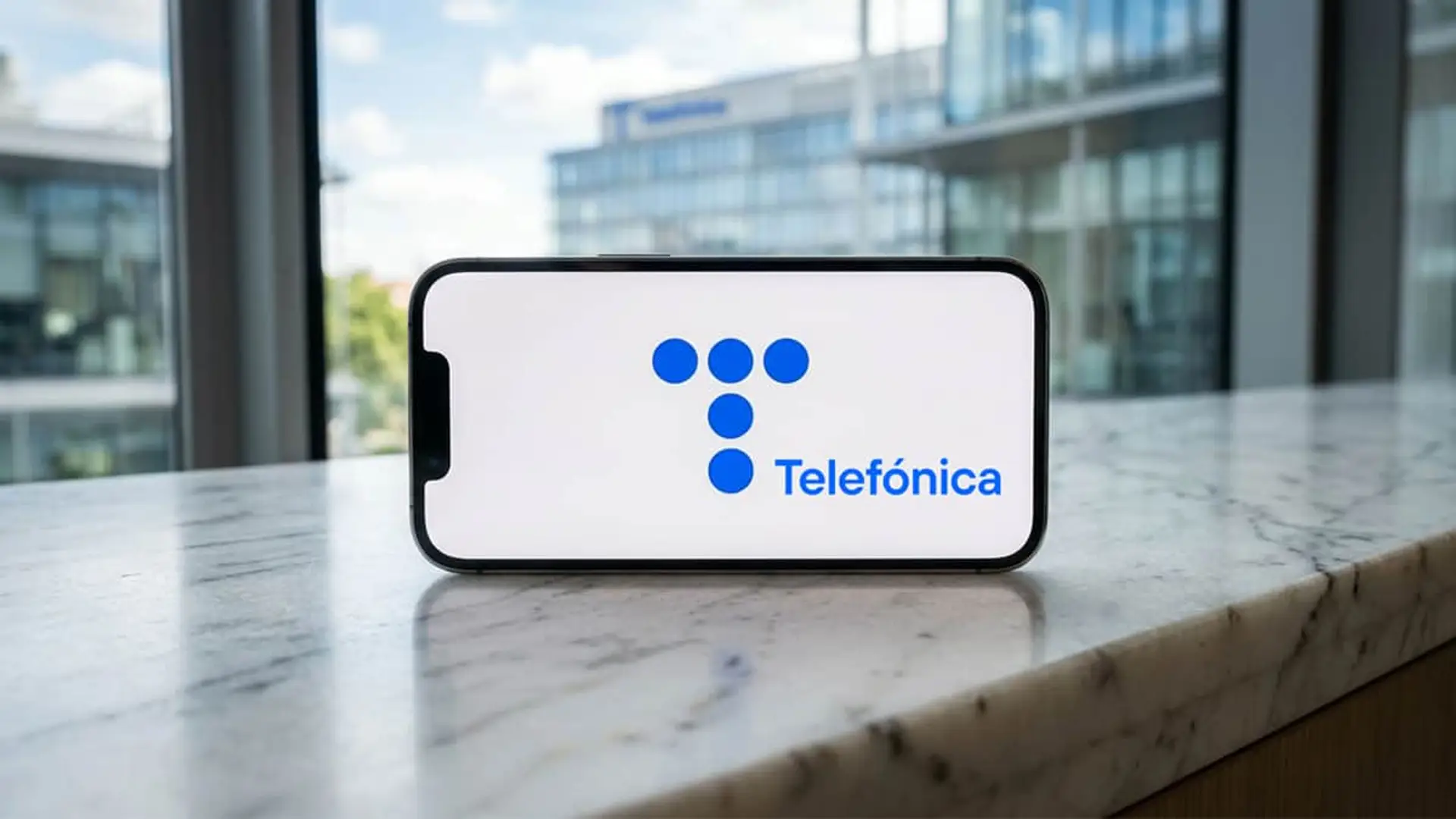 Móvil con el logo de Telefónica sobre una mesa de mármol frente a una oficina acristalada.
