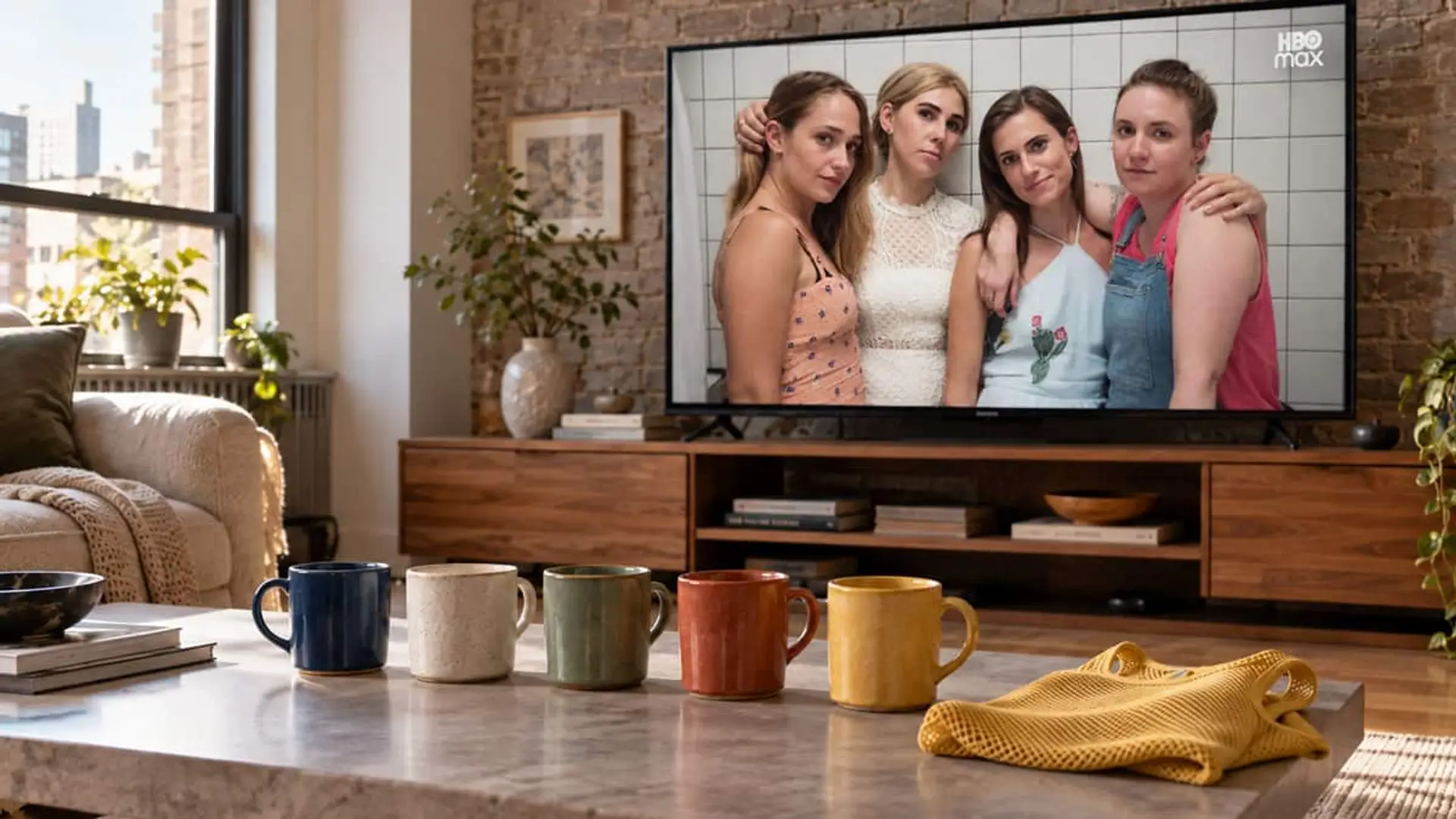 Girls vuelve a HBO diez años después de su final con cinco episodios nuevos y casi todo su reparto Televisor mostrando a cuatro protagonistas de la serie Girls de HBO Max, con cinco tazas de cerámica de distintos colores y una prenda amarilla sobre la mesa de un salón.
